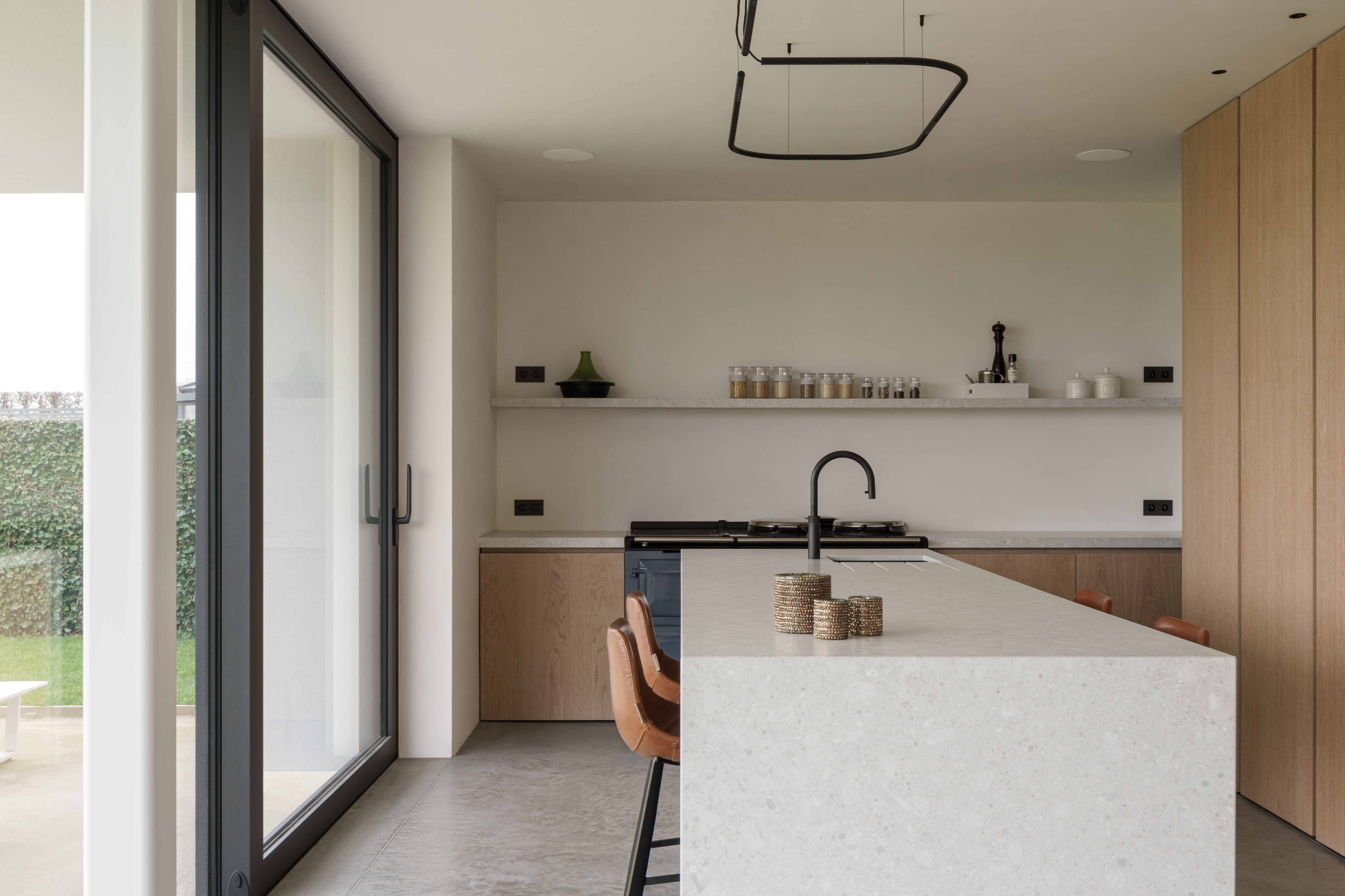 Moderne nieuwbouwwoning met zwart aluminium ALU Ultraglide Monorail-schuifraam naast een minimalistische keuken met kookeiland en houten kasten.