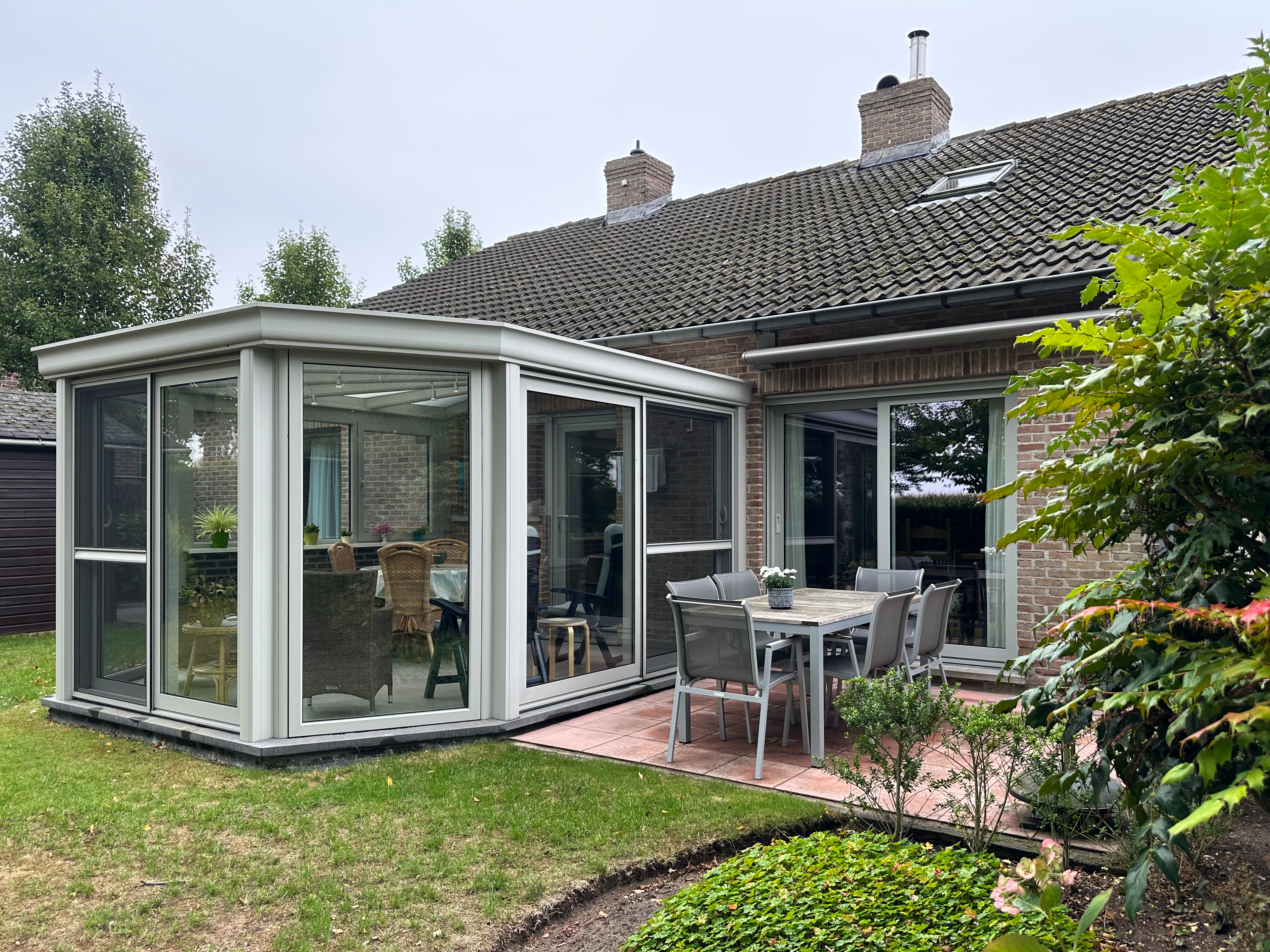 Agaatgrijze aluminium veranda aan een woning, met grote glaspartijen, een schuifraam met ALU Visoglide Duorail en terrasmeubilair.