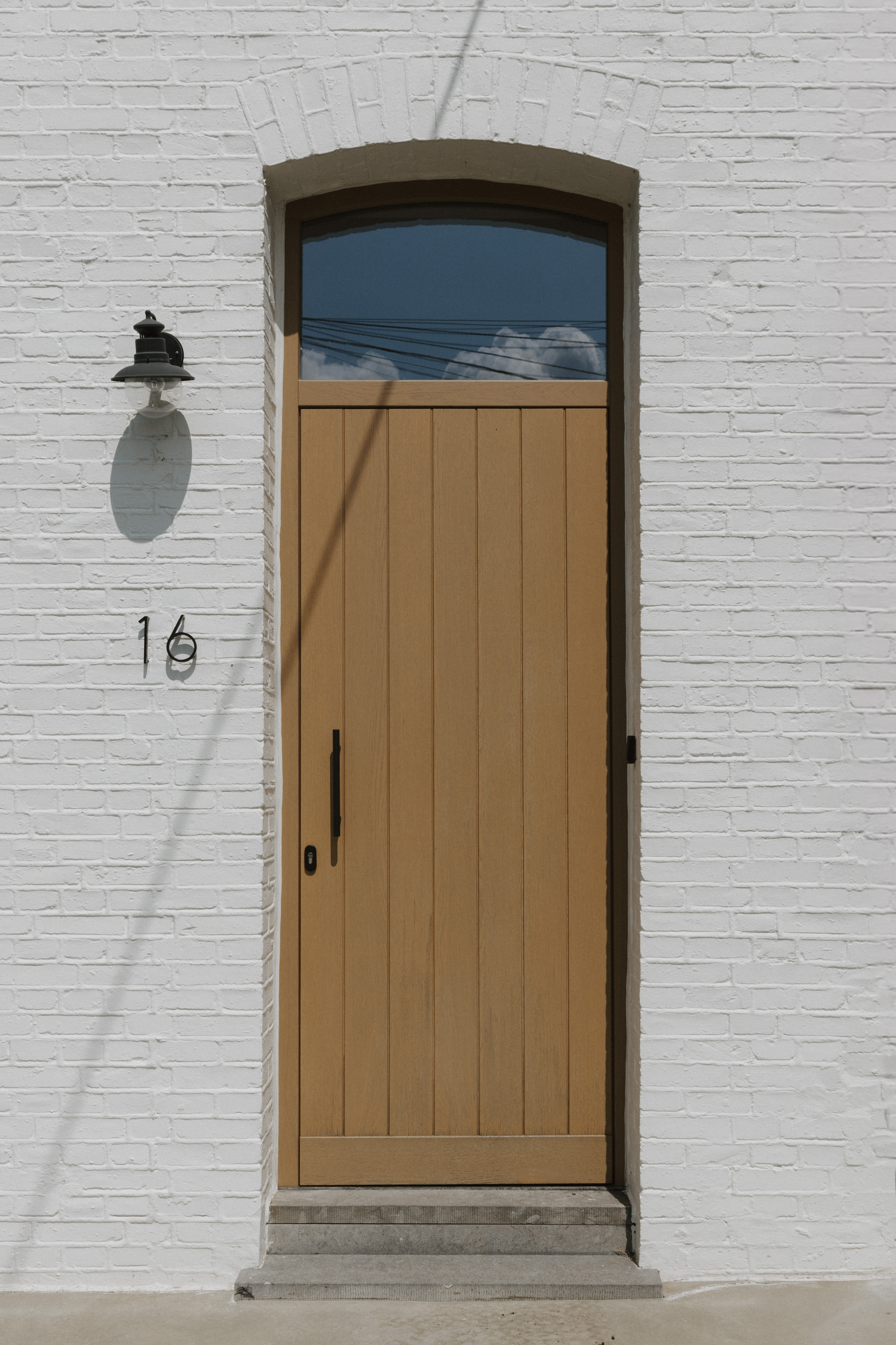 Eiken paneeldeur met bovenlicht in Rubio Natural-afwerking, geplaatst in een witte gevel, met donker beslag en een stenen dorpel.