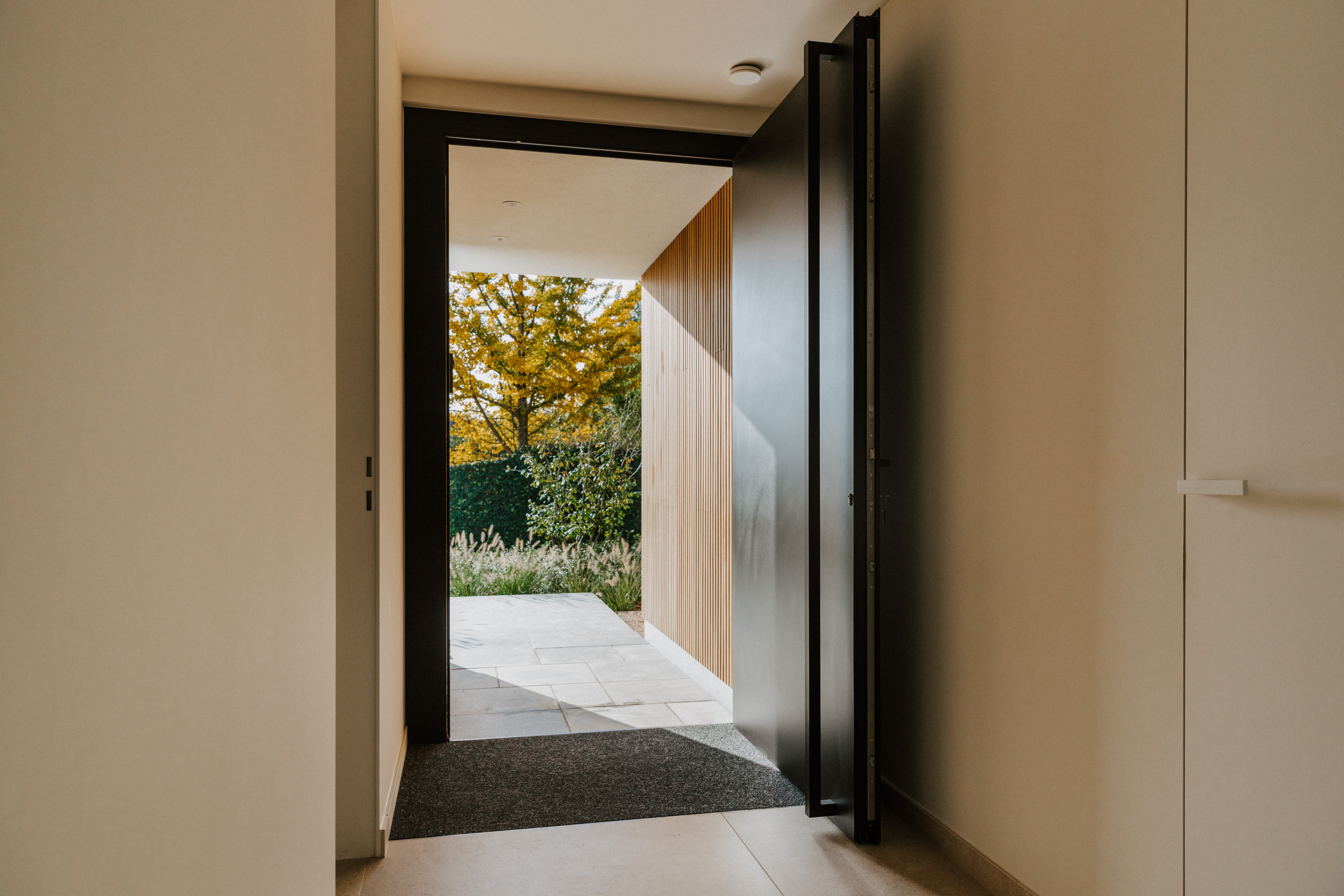Moderne gerenoveerde inkom met geopende zwarte aluminium paneeldeur van ALU Koncept PLUS in signaalzwart, met zicht op het terras.