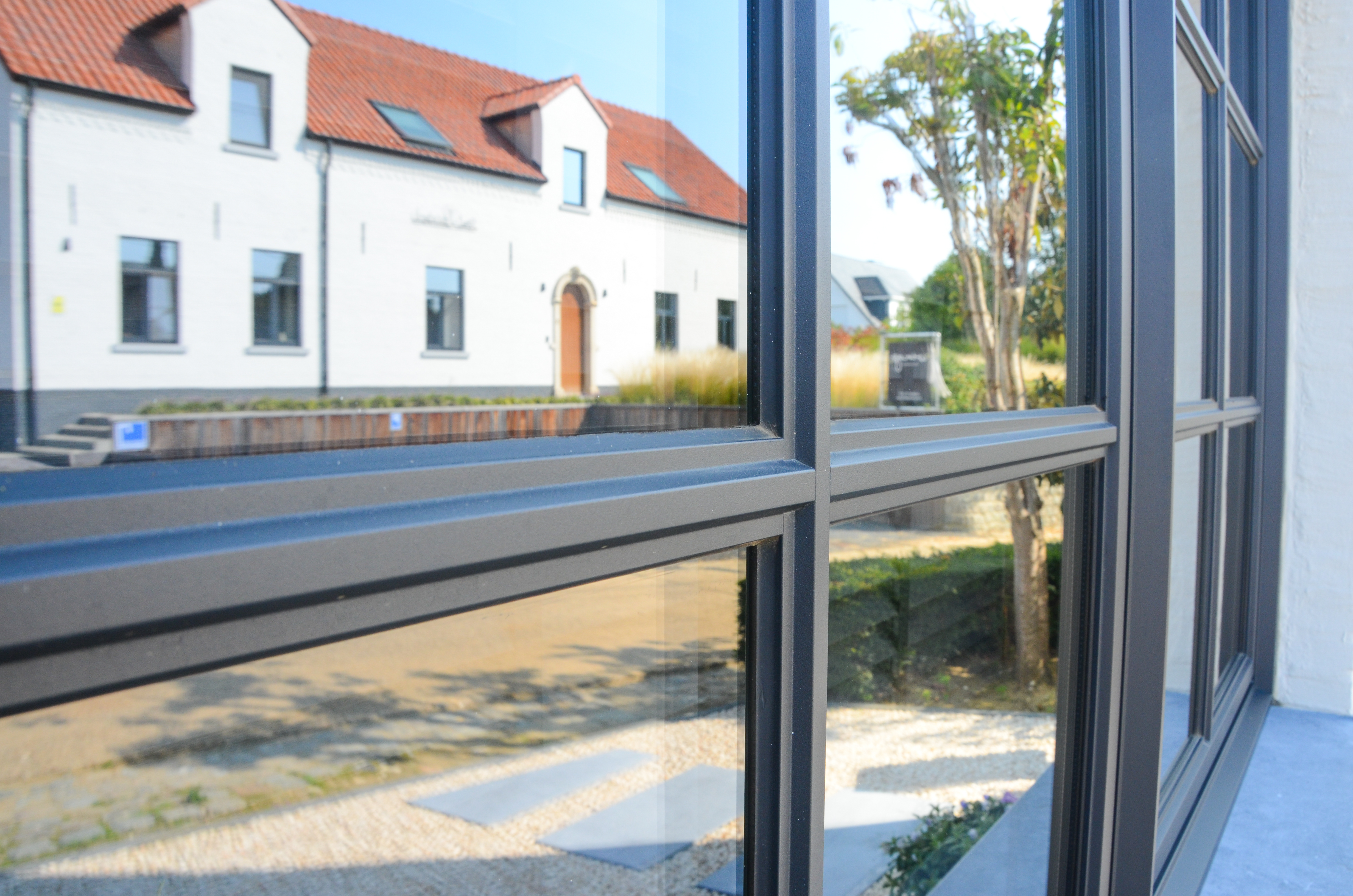 Zwart Steellook PLUS-dubbel raam met draai-kipfunctie in een landelijke woning, met uitzicht op een tegenoverliggende gevel en tuin.