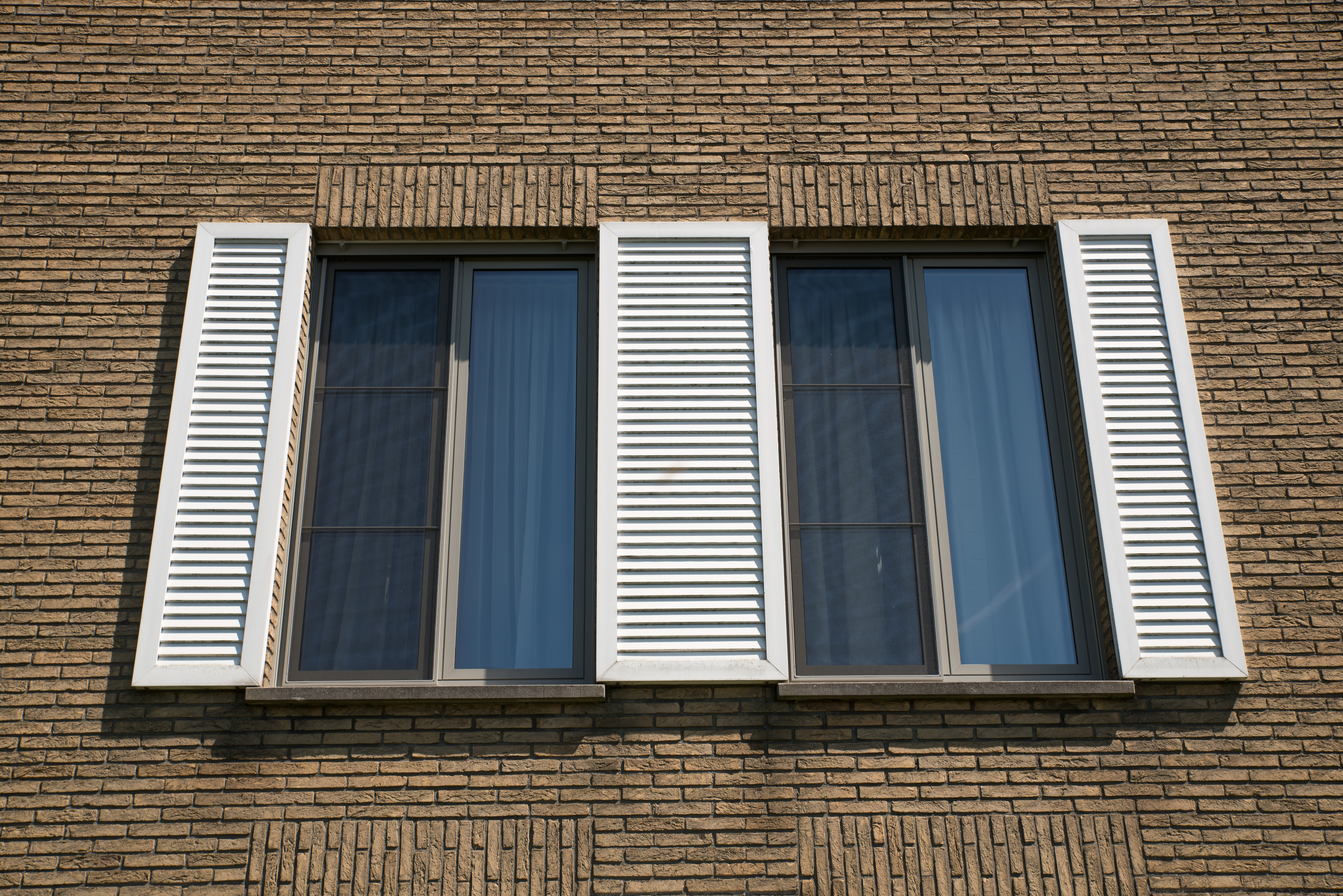 Gerestaureerde bakstenen gevel van een driegevelwoning met twee hoge ramen, donkere raamprofielen en witte luiken met lamellen.