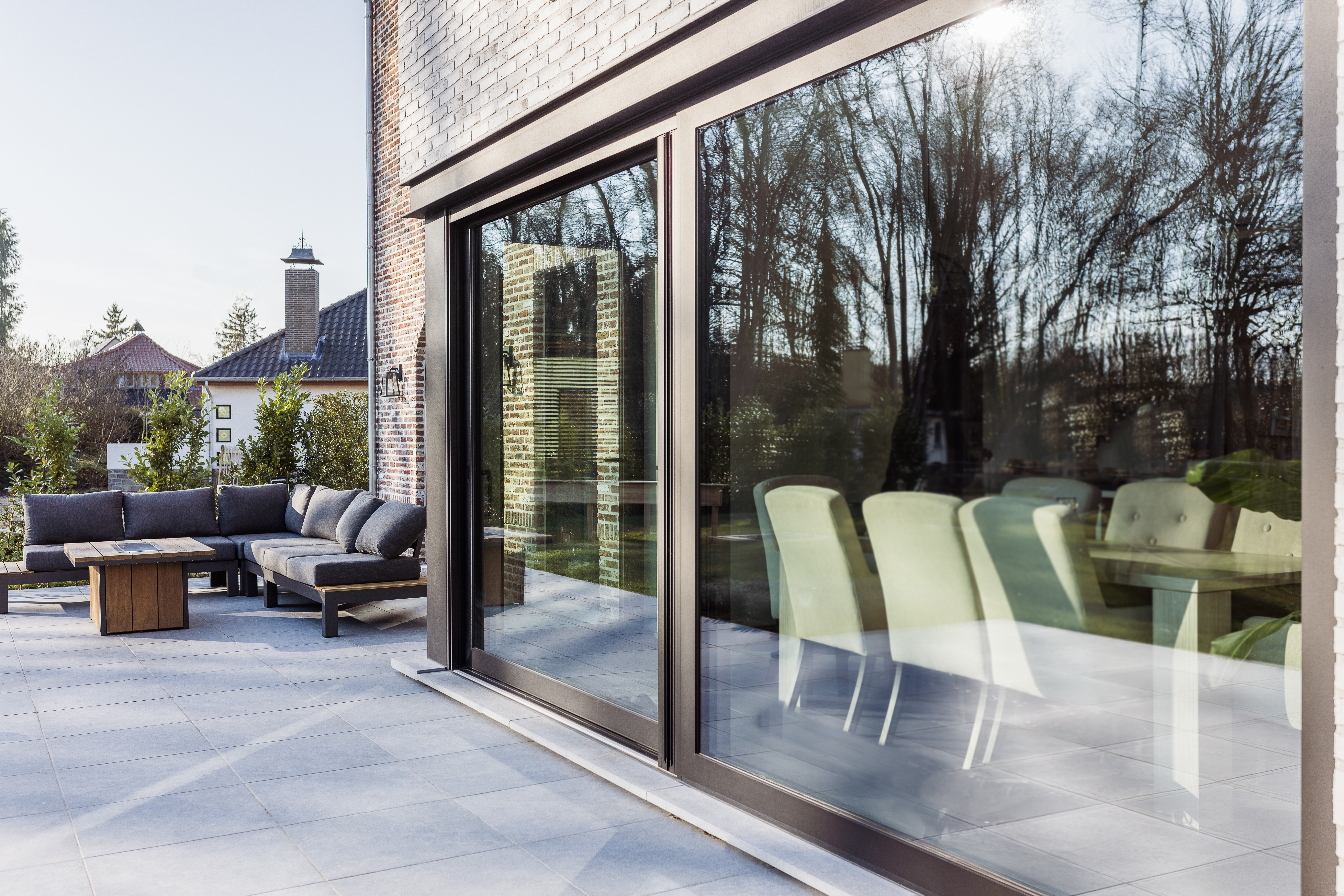 Zwart mat aluminium ALU Visoglide Duorail-schuifraam in een bakstenen gevel, met zicht op het terras en een lichte eetruimte binnen.