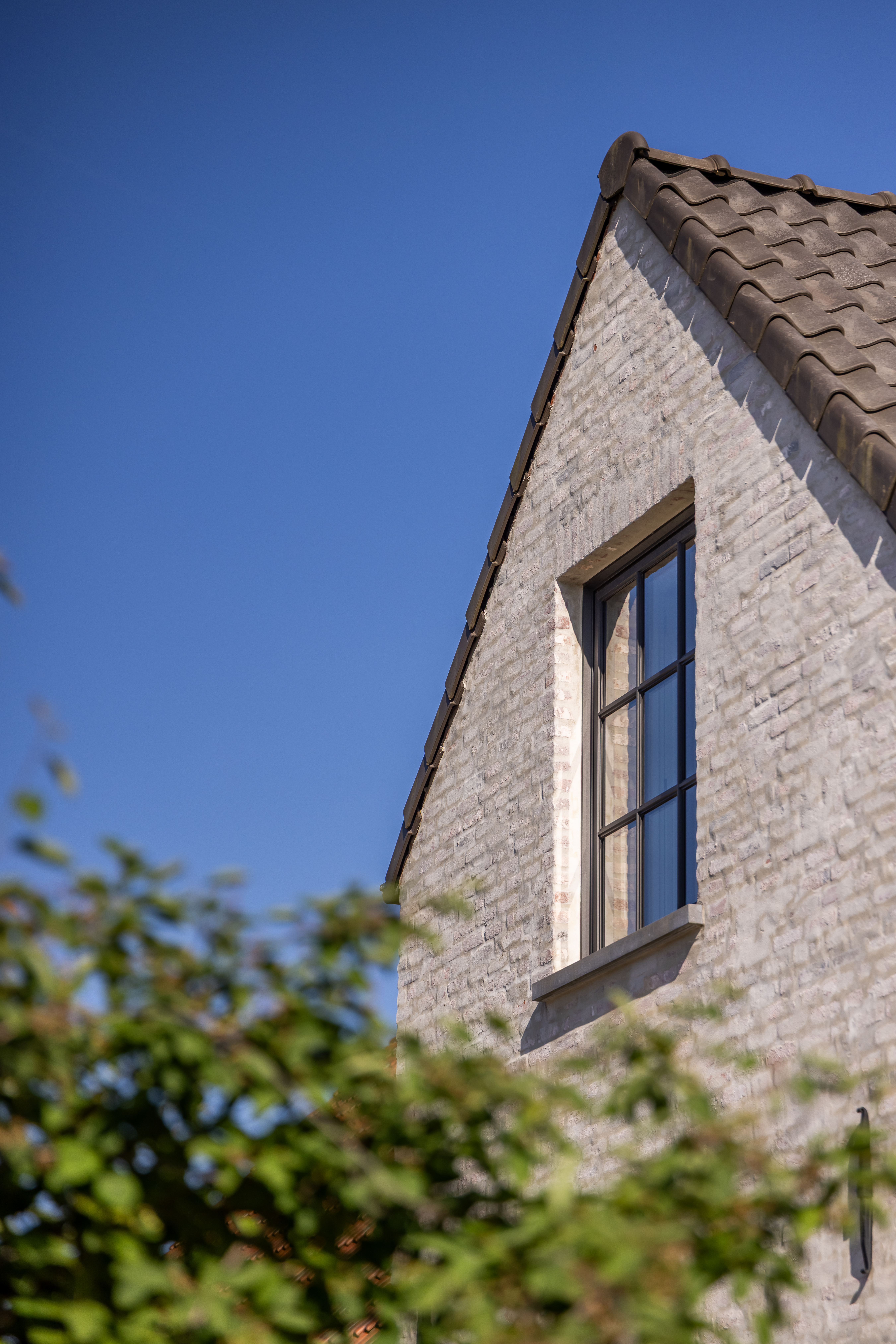 Lichte bakstenen puntgevel van een vrijstaande woning in warme landelijke stijl, met een zwart Steellook PLUS small raam in vaste en draai-kipuitvoering.