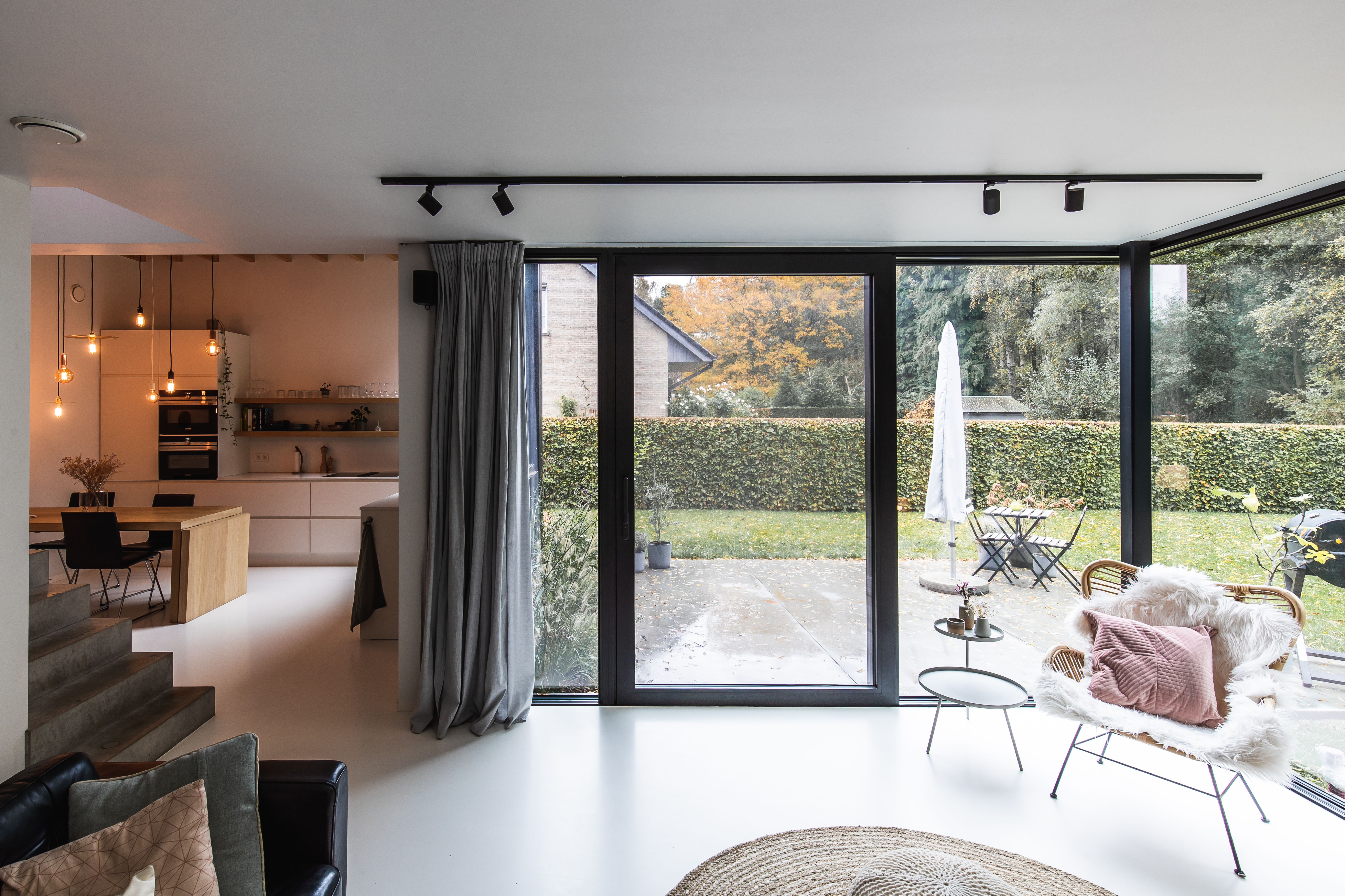 Modern interieur van een nieuwbouwwoning met zwart aluminium schuifraam ALU Visoglide Monorail in 9005TC, dat de leefruimte met de tuin van de open bebouwing verbindt.