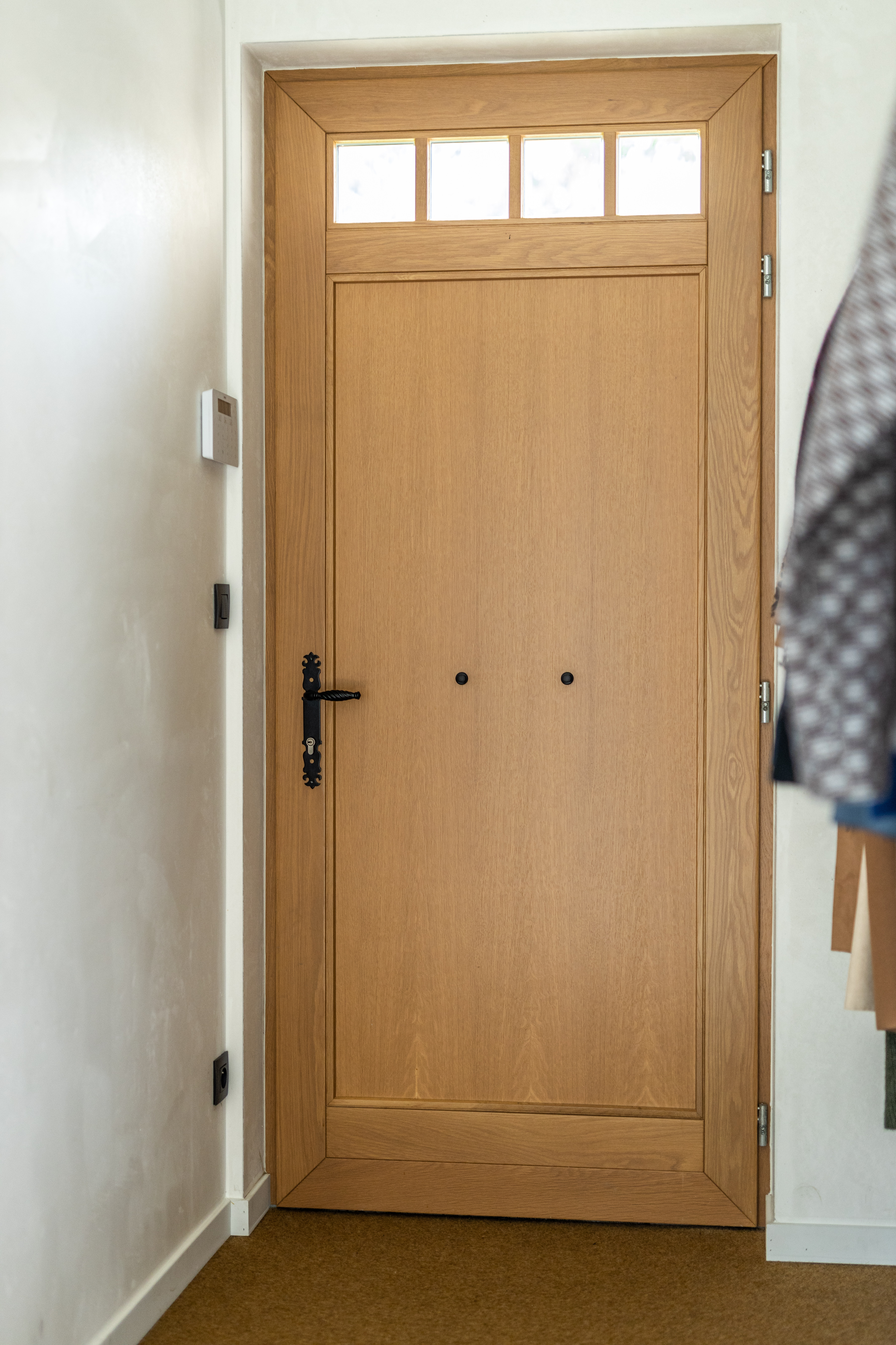 Gelakte mahoniedeur met eikenhouten details en bovenlicht in een warme, landelijke inkomhal van een vrijstaande nieuwbouwwoning.