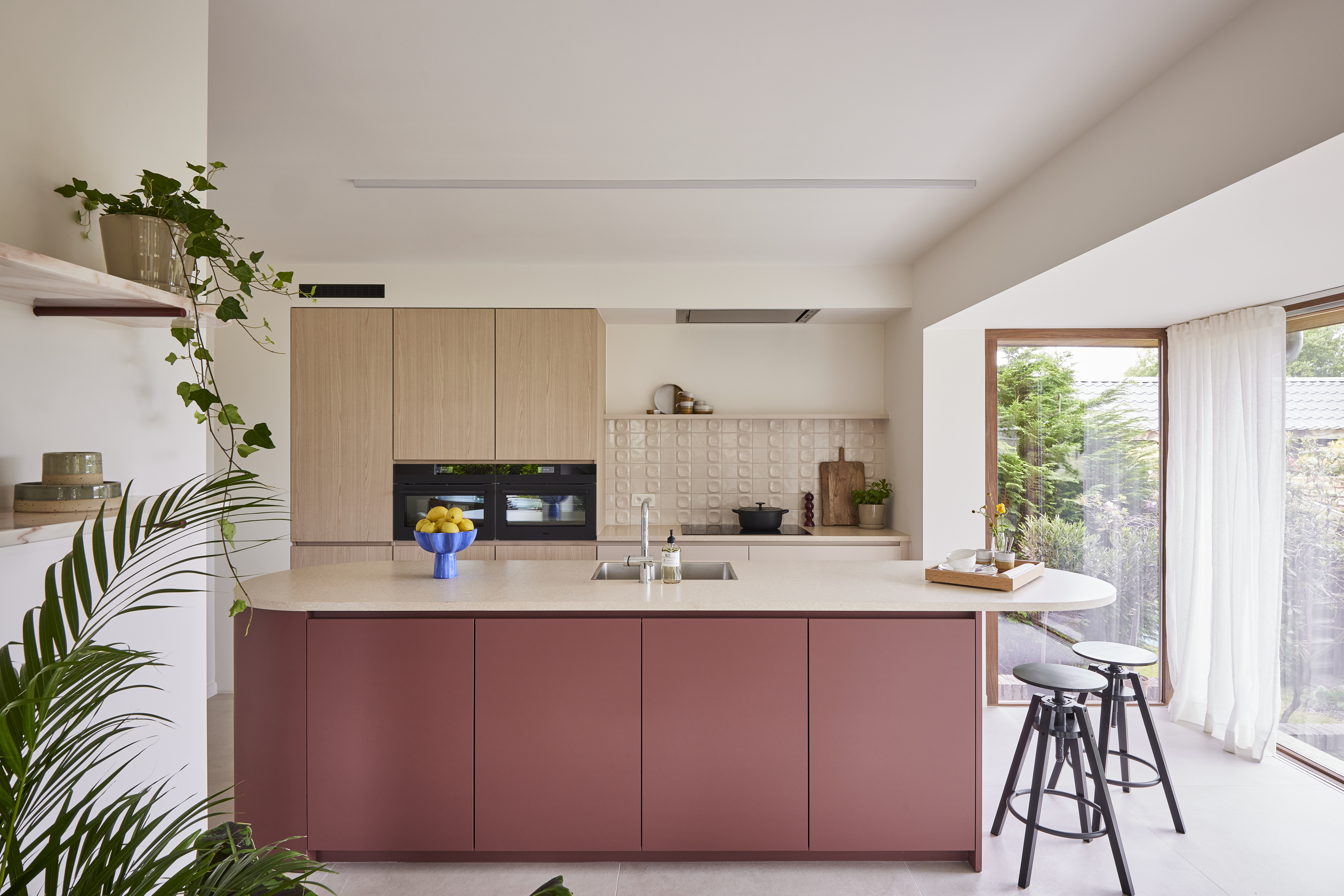 Modern vast raam met een natuurlijk houten raamprofiel in een lichte keuken, naast witte gordijnen en een oudroze keukeneiland.