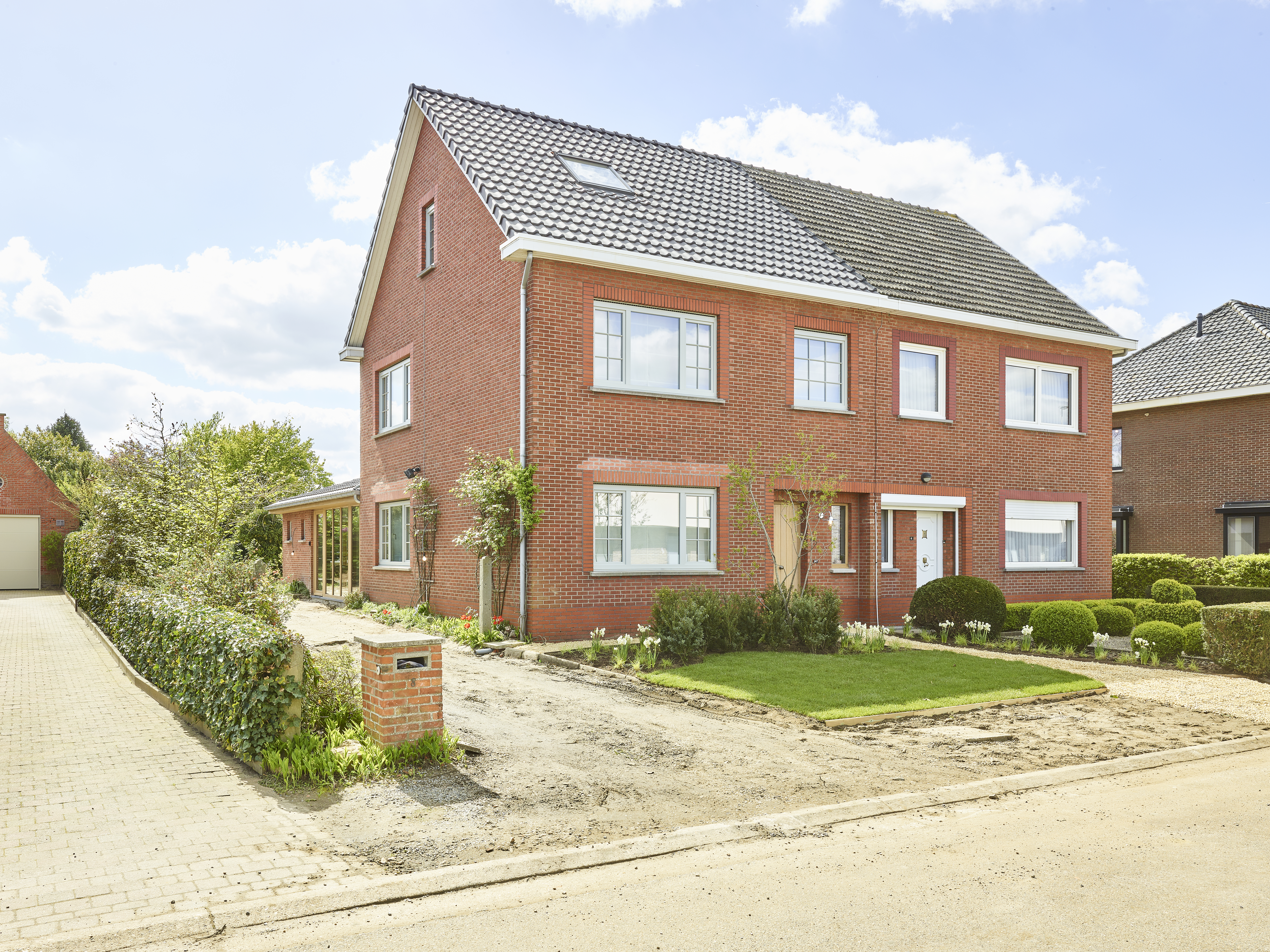 Rood bakstenen huis met lichte draai-kipramen en raamprofielen in een warme, landelijke stijl, omgeven door een verzorgde voortuin en een verharde oprit.