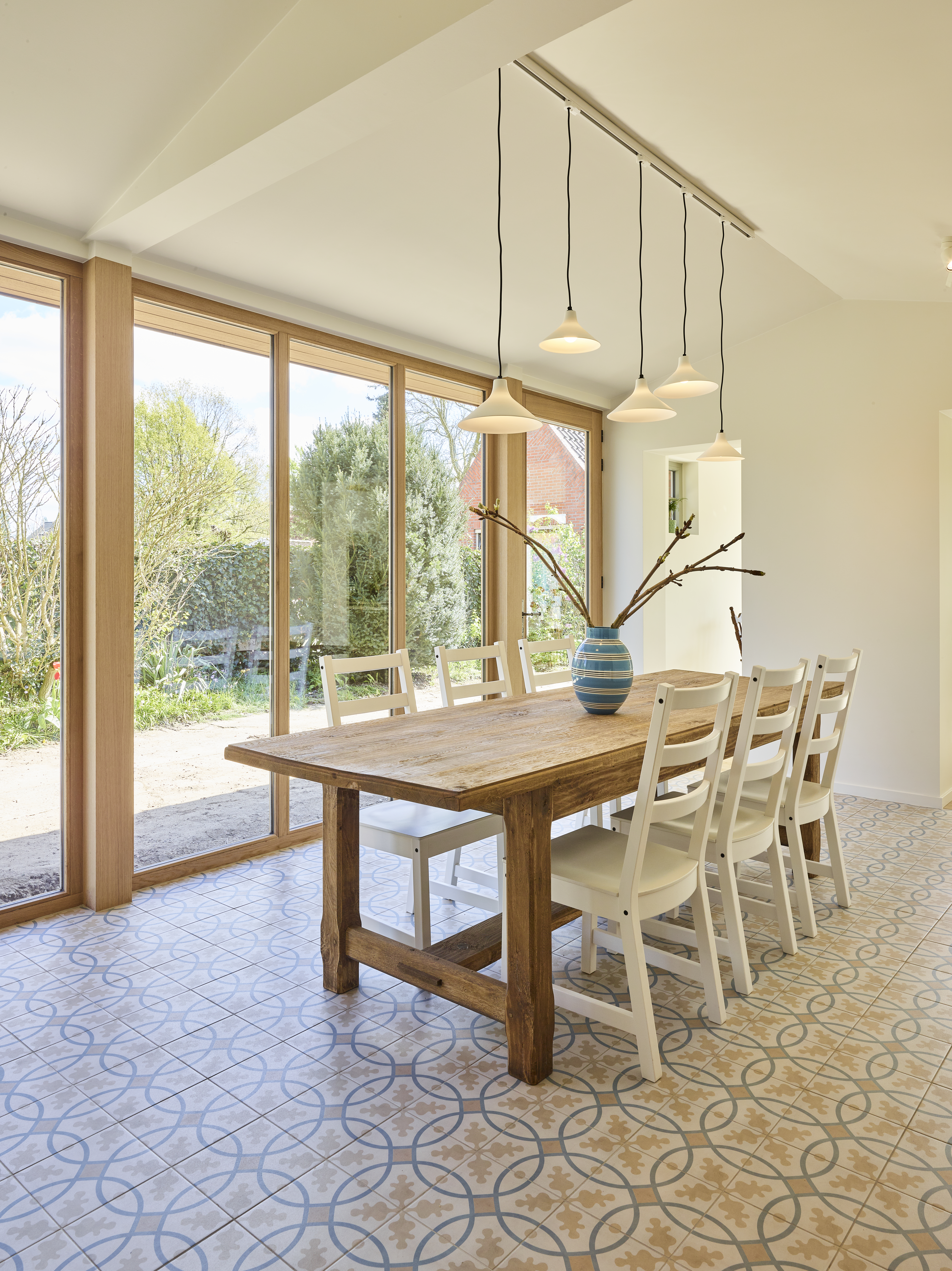 Moderne, warme landelijke eetruimte met raamprofielen in afgelakte lichte eik, driedubbele beglazing en een vast raam naast een houten eettafel.
