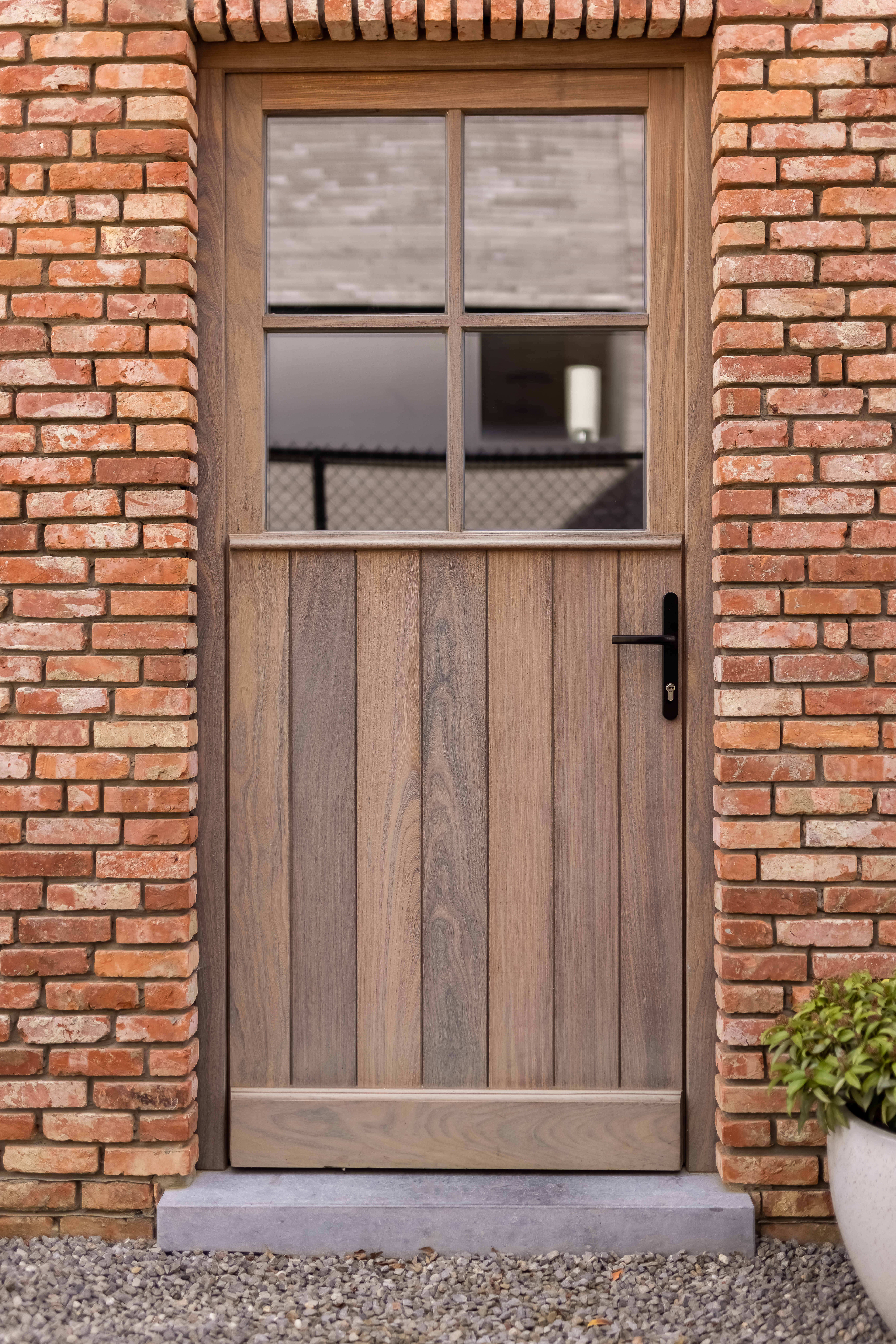 Semi-beglaasde voordeur in Afrormosia-hout met een natuurlijke Rubio Natural-afwerking, omlijst door een bakstenen gevel in een warme landelijke stijl.