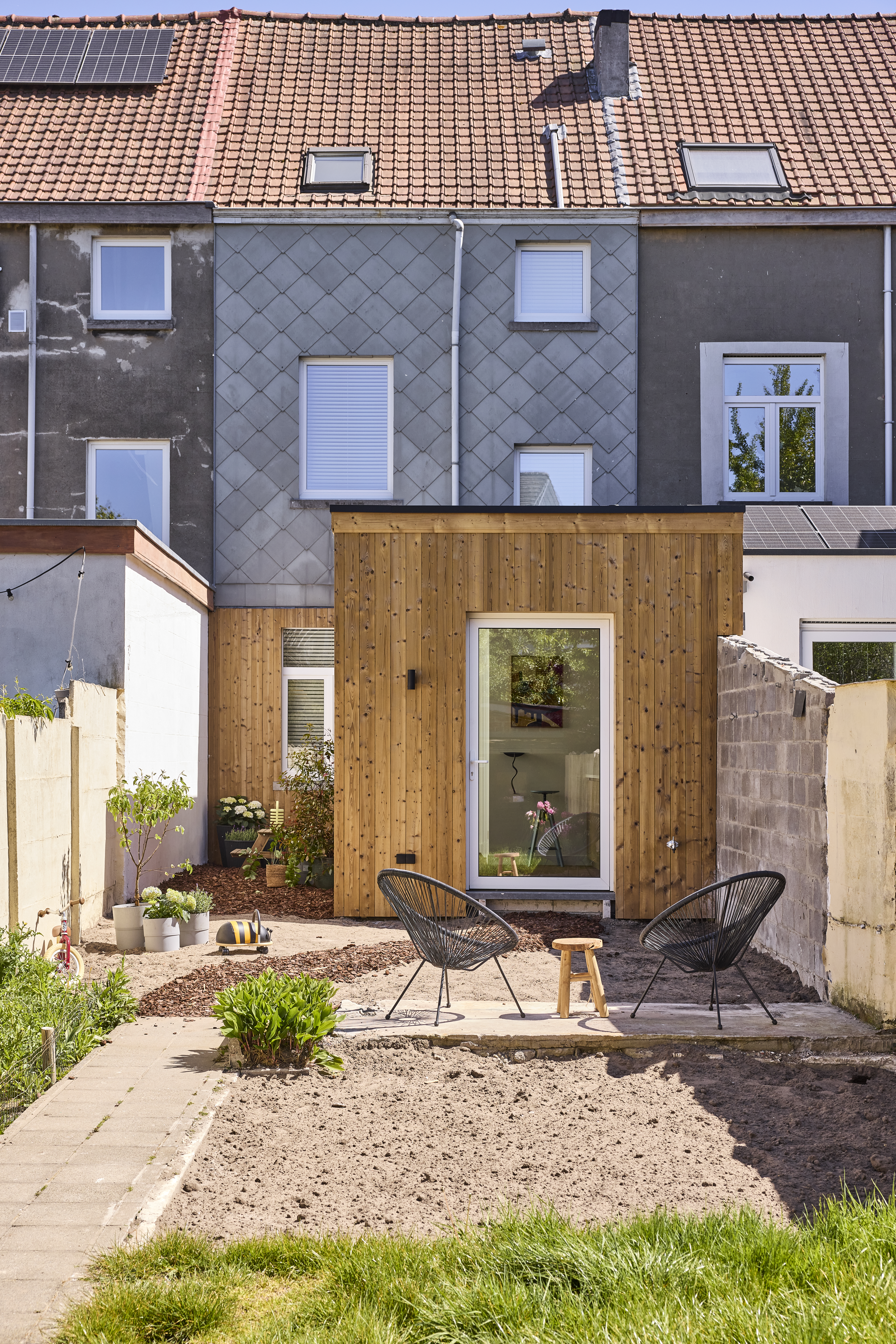 Woning met donkere gevelbekleding, witte ALU Komfort EVO-draai-kipramen en een beglaasde deur in een houten aanbouw.