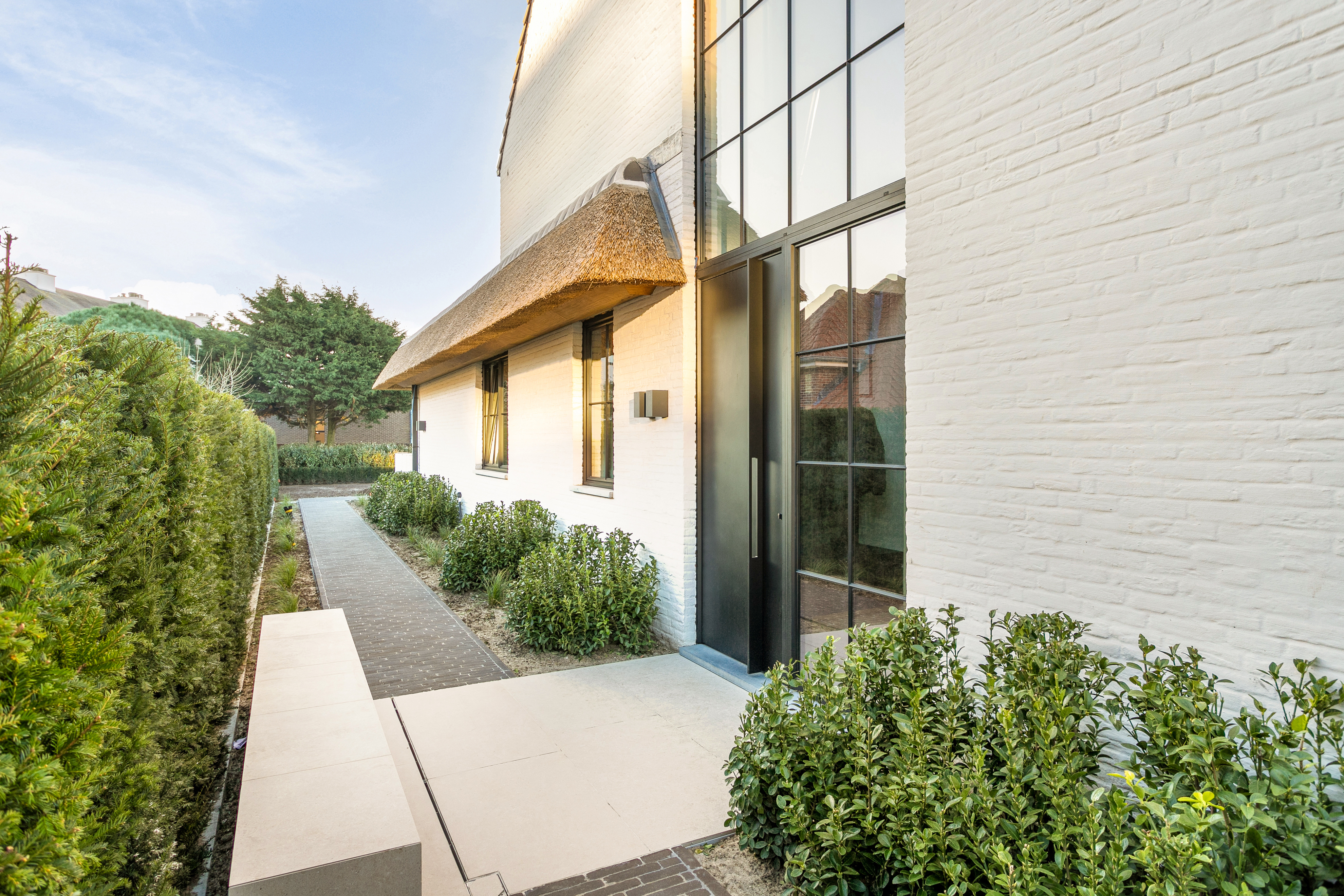 Vast ALU-raam in zwarte Steellook PLUS-stijl, geïntegreerd in een lichte bakstenen gevel naast de inkom van een moderne woning.