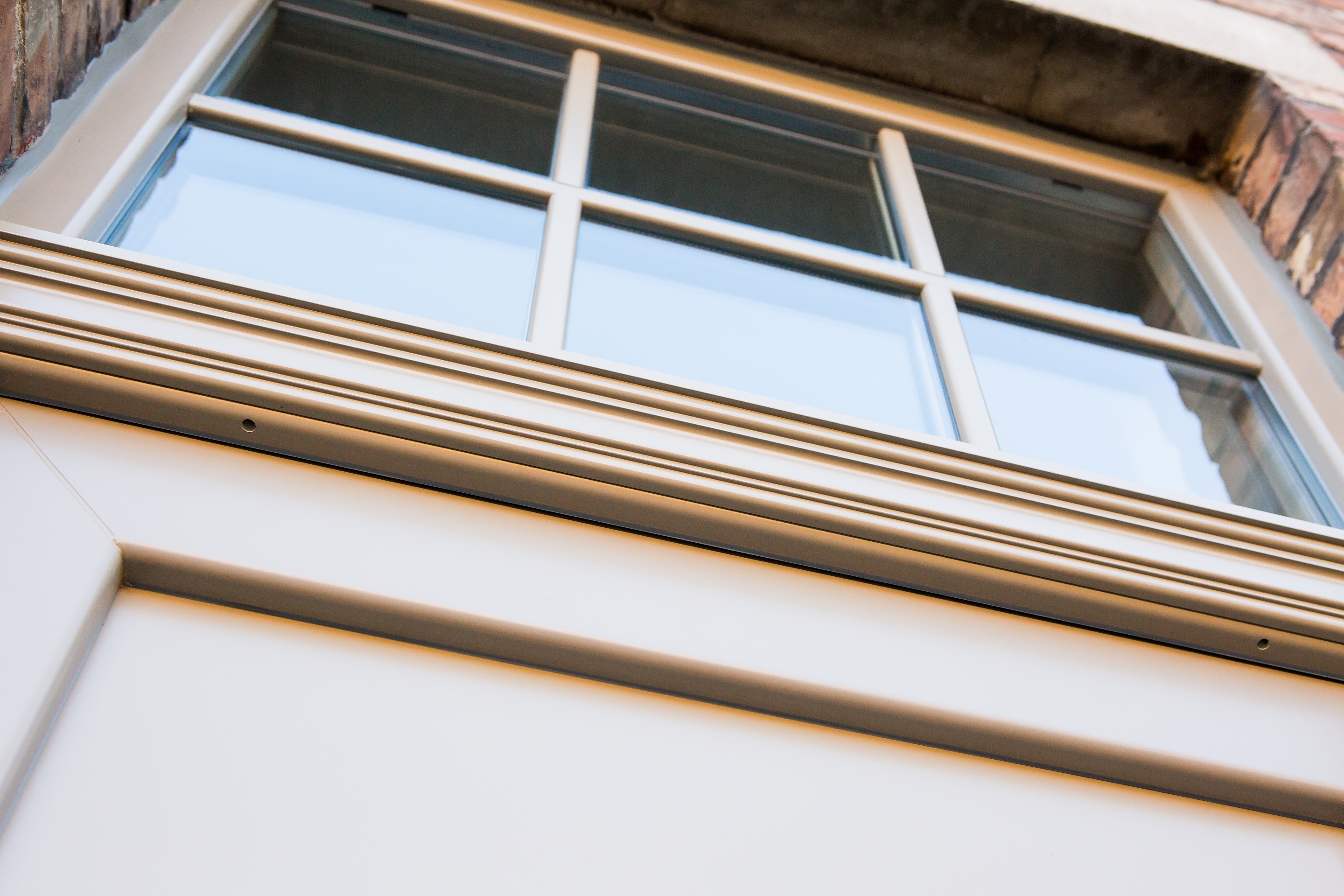 Klassieke voordeur met bovenlicht en paneel in een gerenoveerde gesloten bebouwing, van onderaf bekeken, met witte profielen en onderverdeelde beglazing.