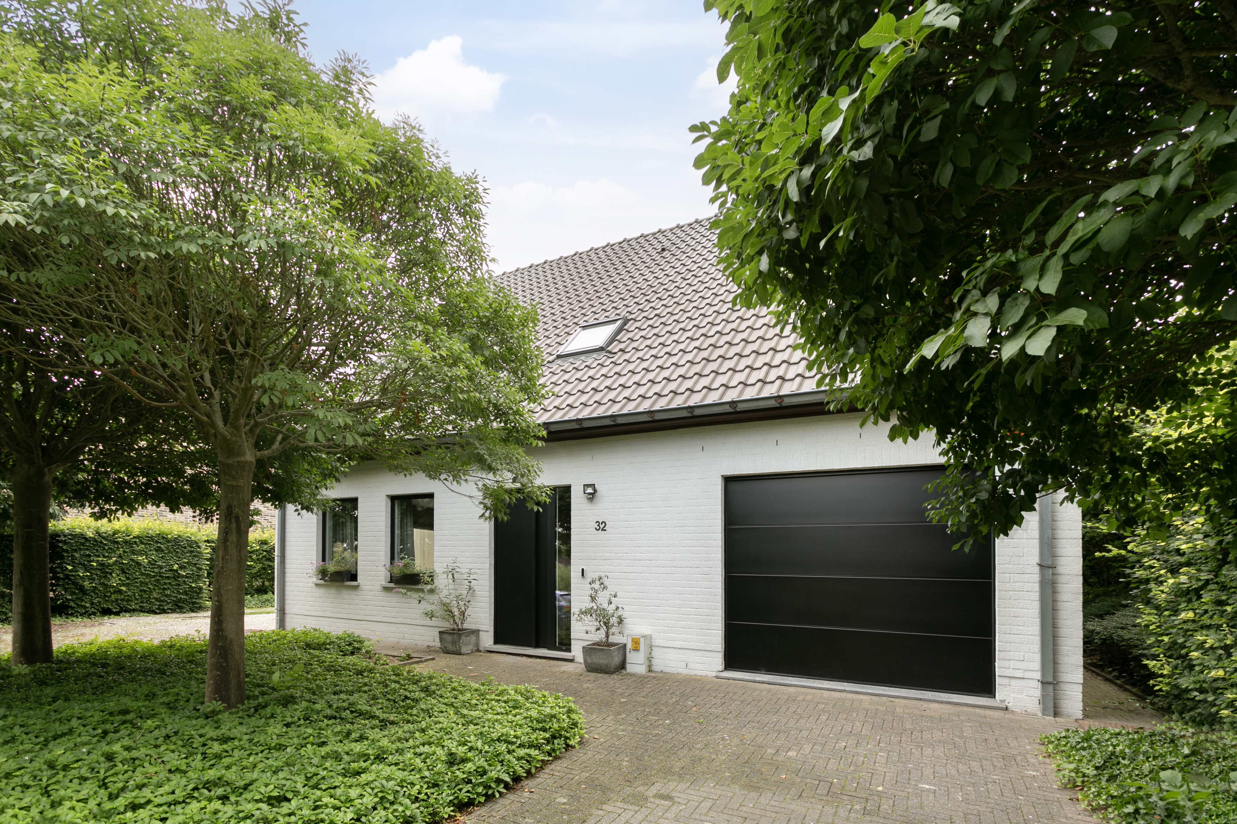 Witte woning met zwarte ALU Koncept-garagepoort in Signaalzwart en zwarte voordeur met zijlicht, omgeven door groen.