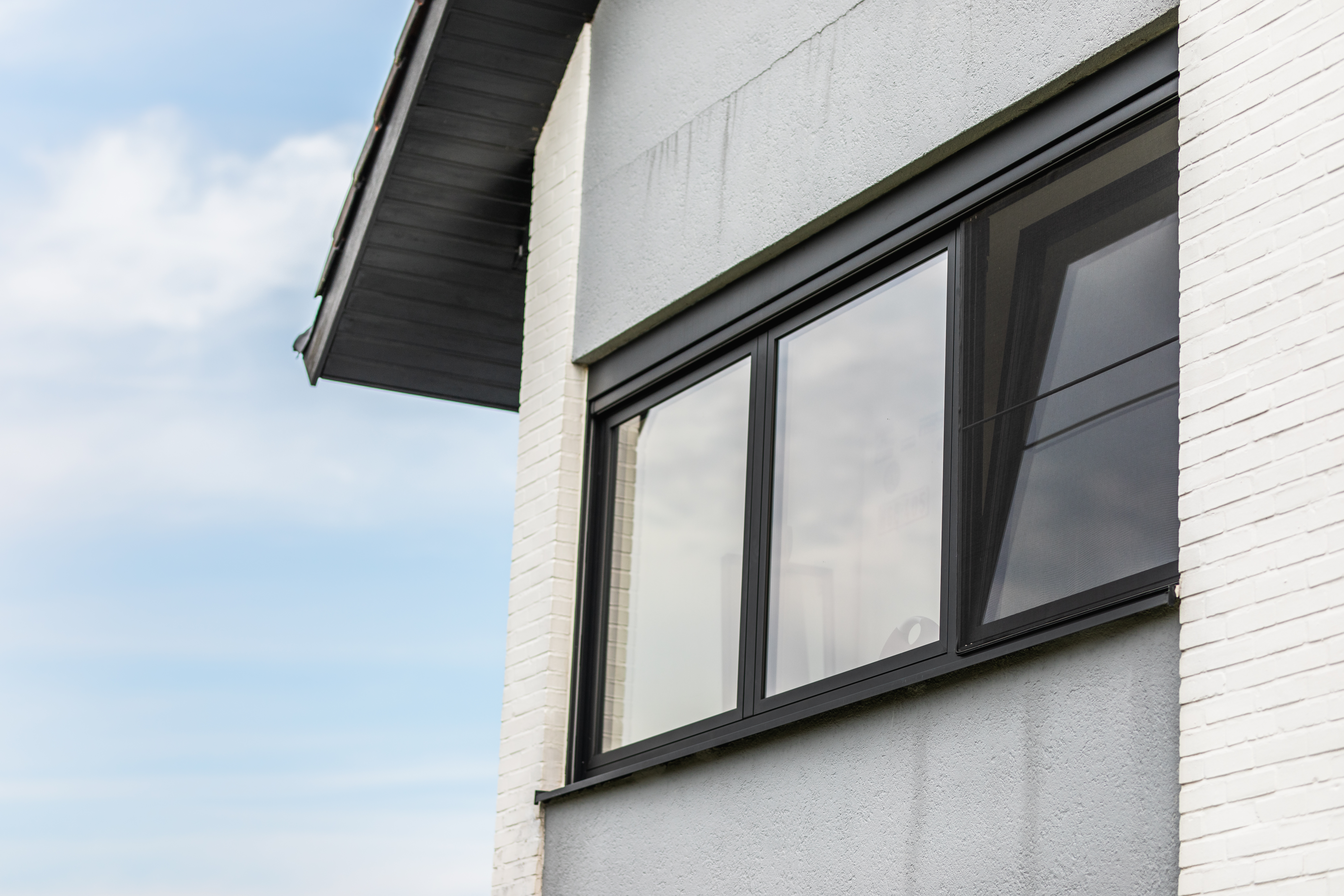 Modern zwart raam met drie verticale delen en draai-kipfunctie in de lichte gevel van een open bebouwing.