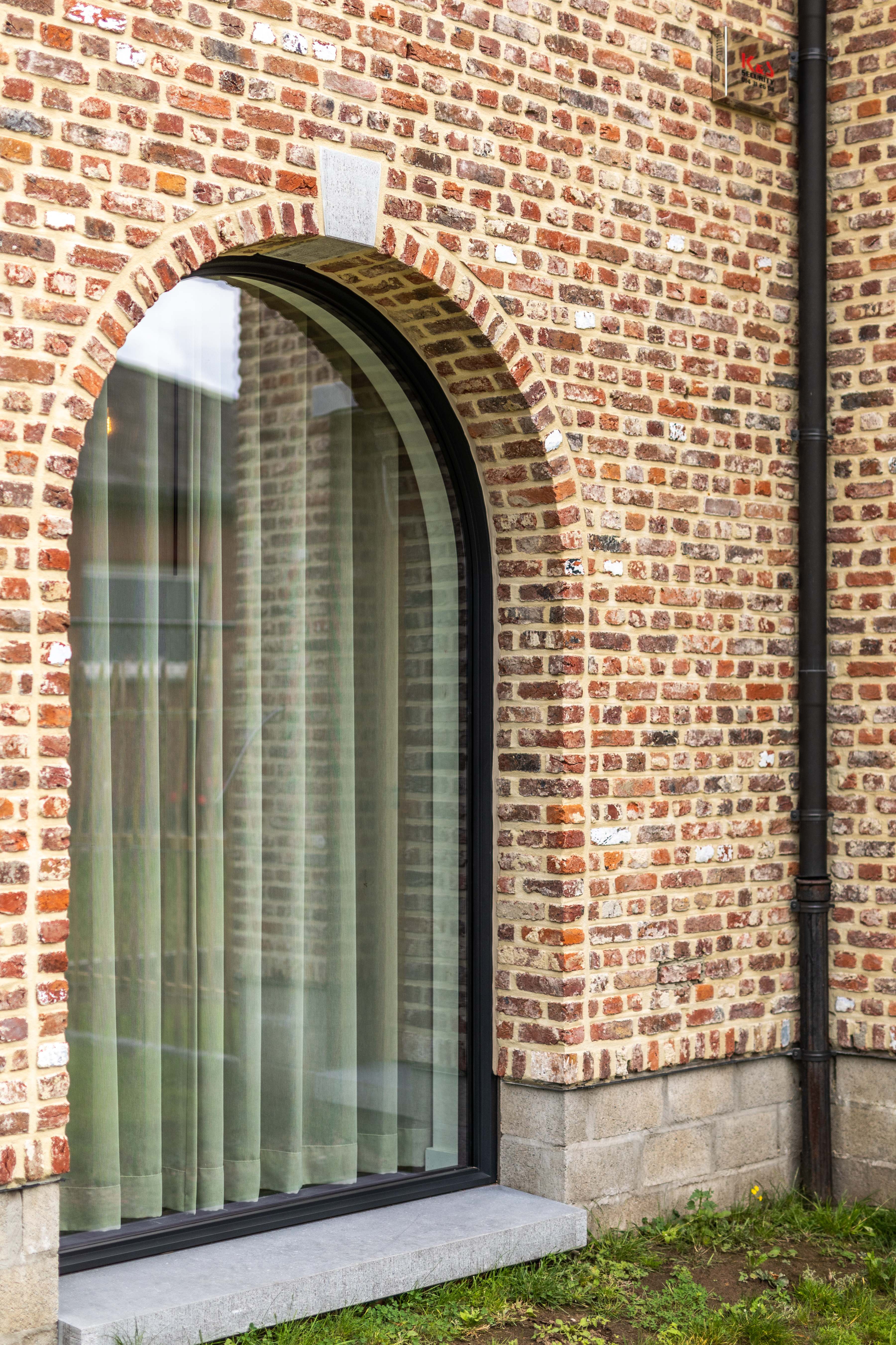 Vast, rondboogvormig raam in zwarte Steellook PLUS-stijl met fijne profielen, geïntegreerd in een warme, landelijke bakstenen gevel van een nieuwbouwwoning.