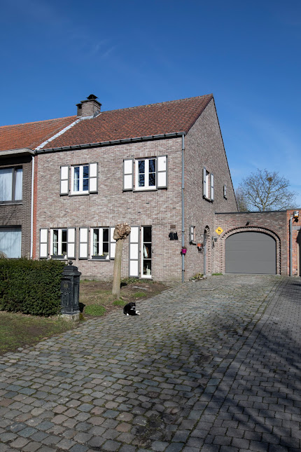 Landelijke gerenoveerde halfopen woning met bakstenen gevel, witte luiken en ramen, rood pannendak, gewelfde garagepoort en gekasseide oprit.