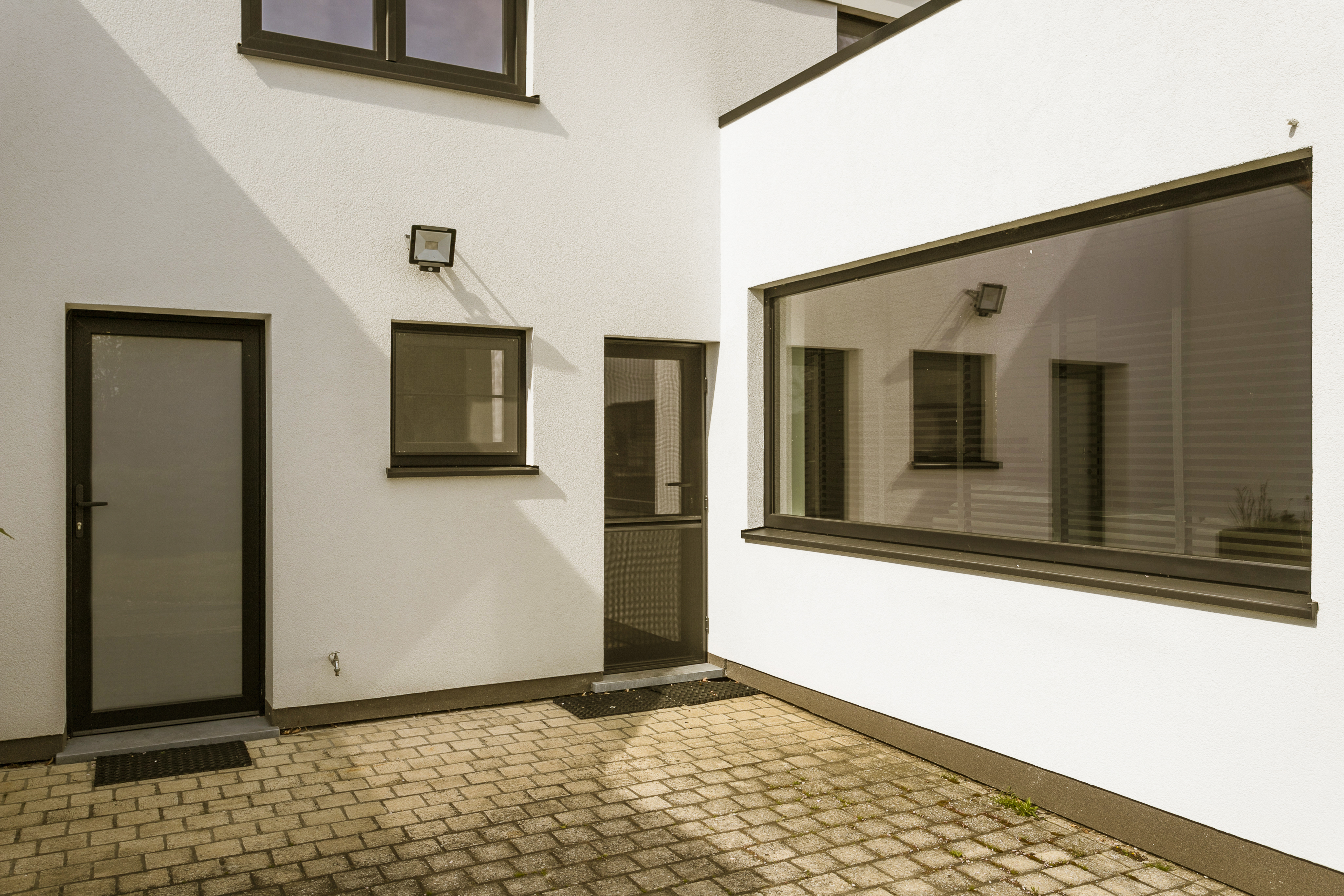Binnenkoer van een gerenoveerde woning met een groot vast raam in matzwarte pvc-profielen en een beglaasde deur.