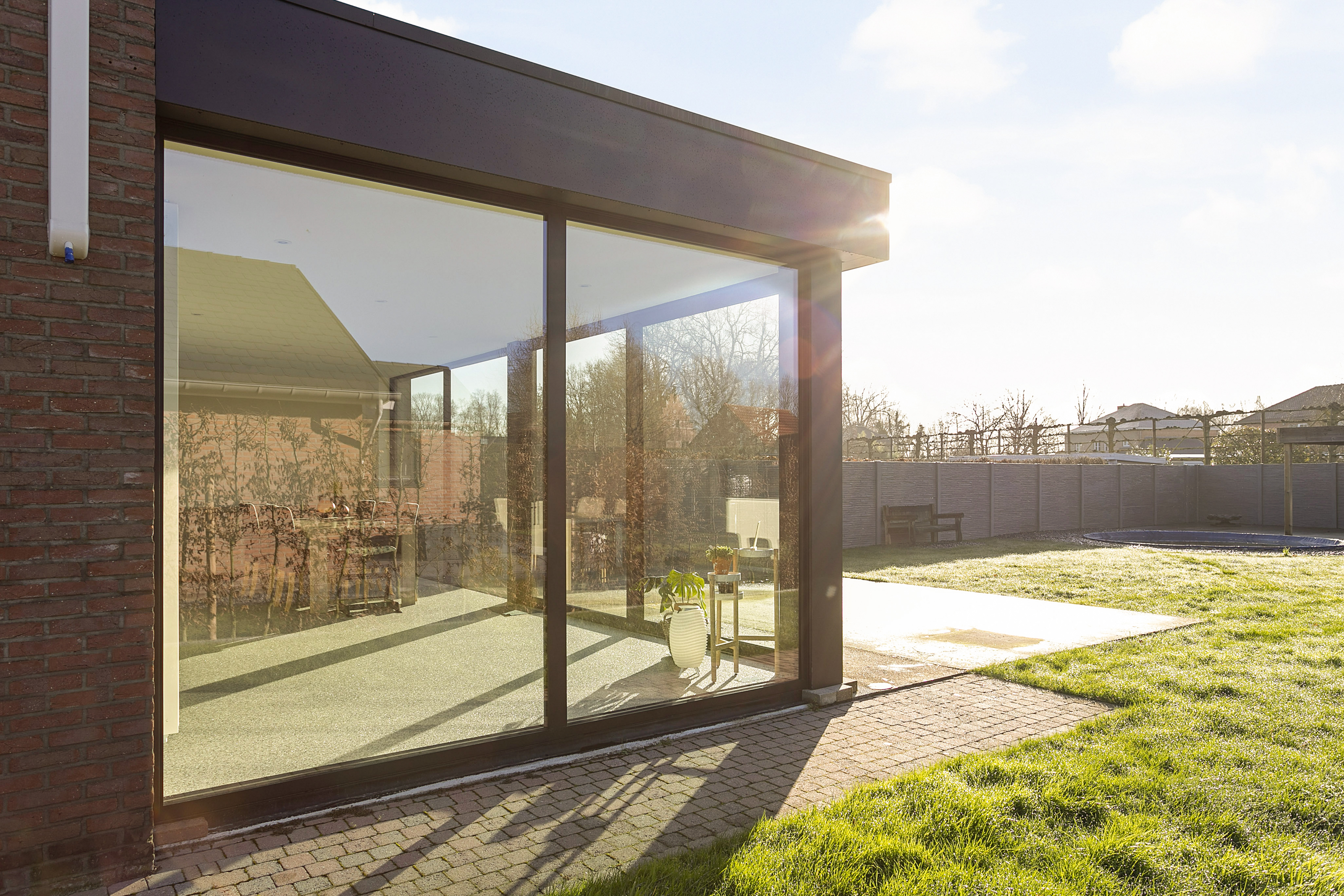 Vast raam met zwarte aluminiumprofielen in een glazen aanbouw van een halfopen bebouwing, naast een terras en een tuin.