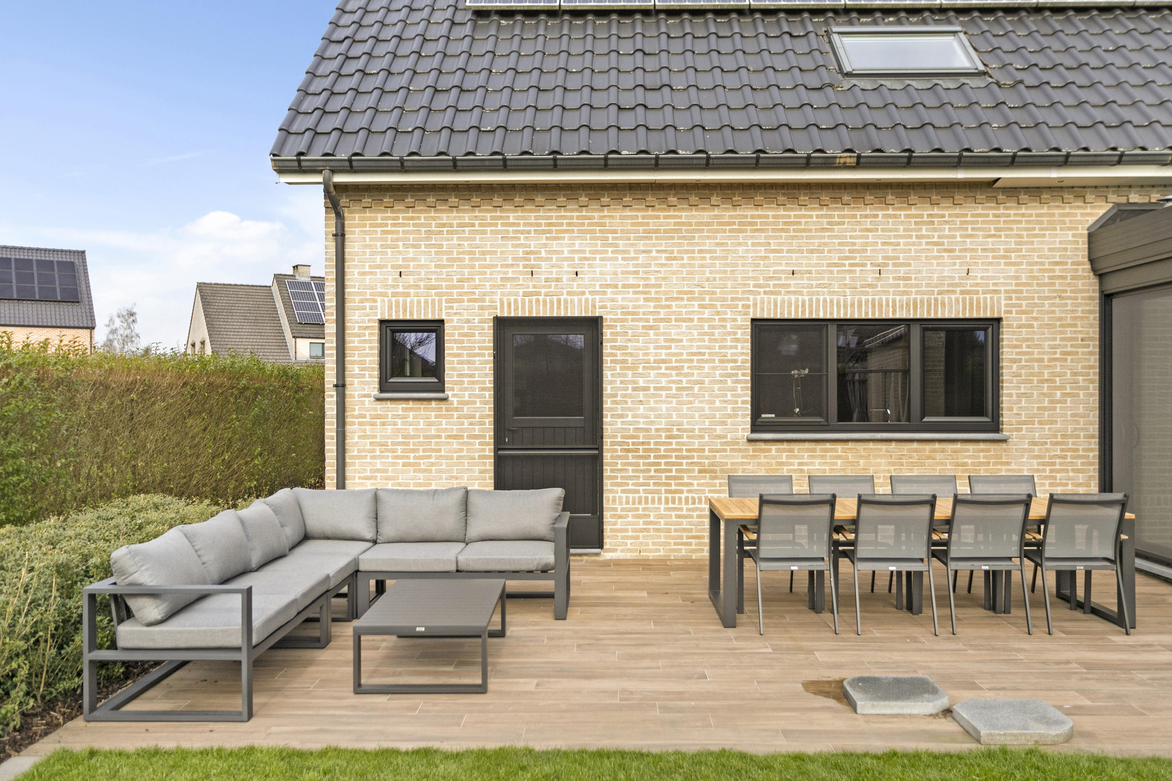 Bakstenen woning met matzwarte PVC-raamprofielen, een semi-beglaasde deur en een draai-kipraam met driedubbele beglazing aan een houten terras.