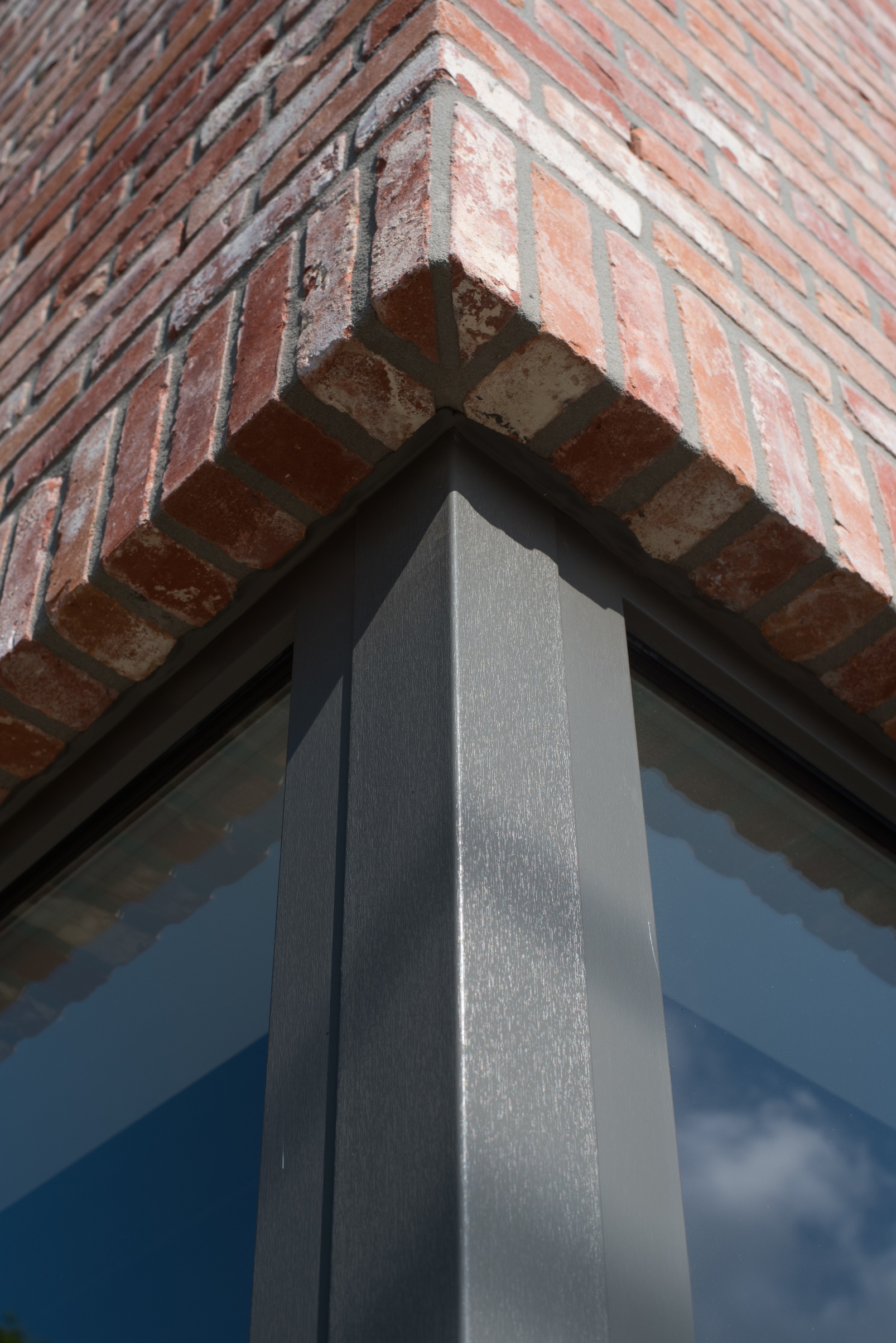 Hoekraam met kwartsgrijze NERF-raamprofielen onder een opvallende bakstenen latei, in de gevel van een tijdloze halfopen nieuwbouwwoning.