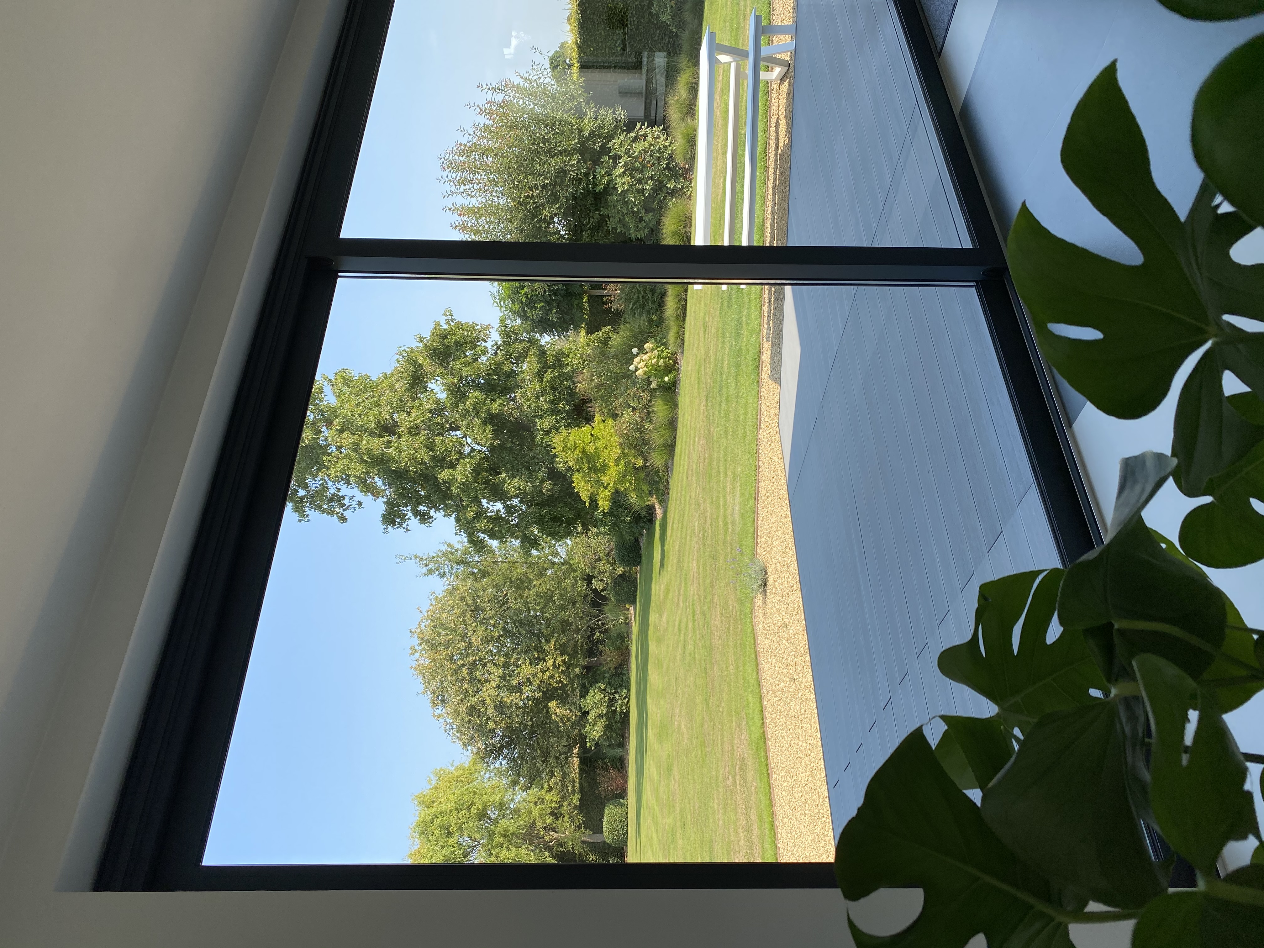 Groot zwart aluminium schuifraam ALU Visoglide Duorail met uitzicht op een terras en de groene tuin van een open bebouwing.