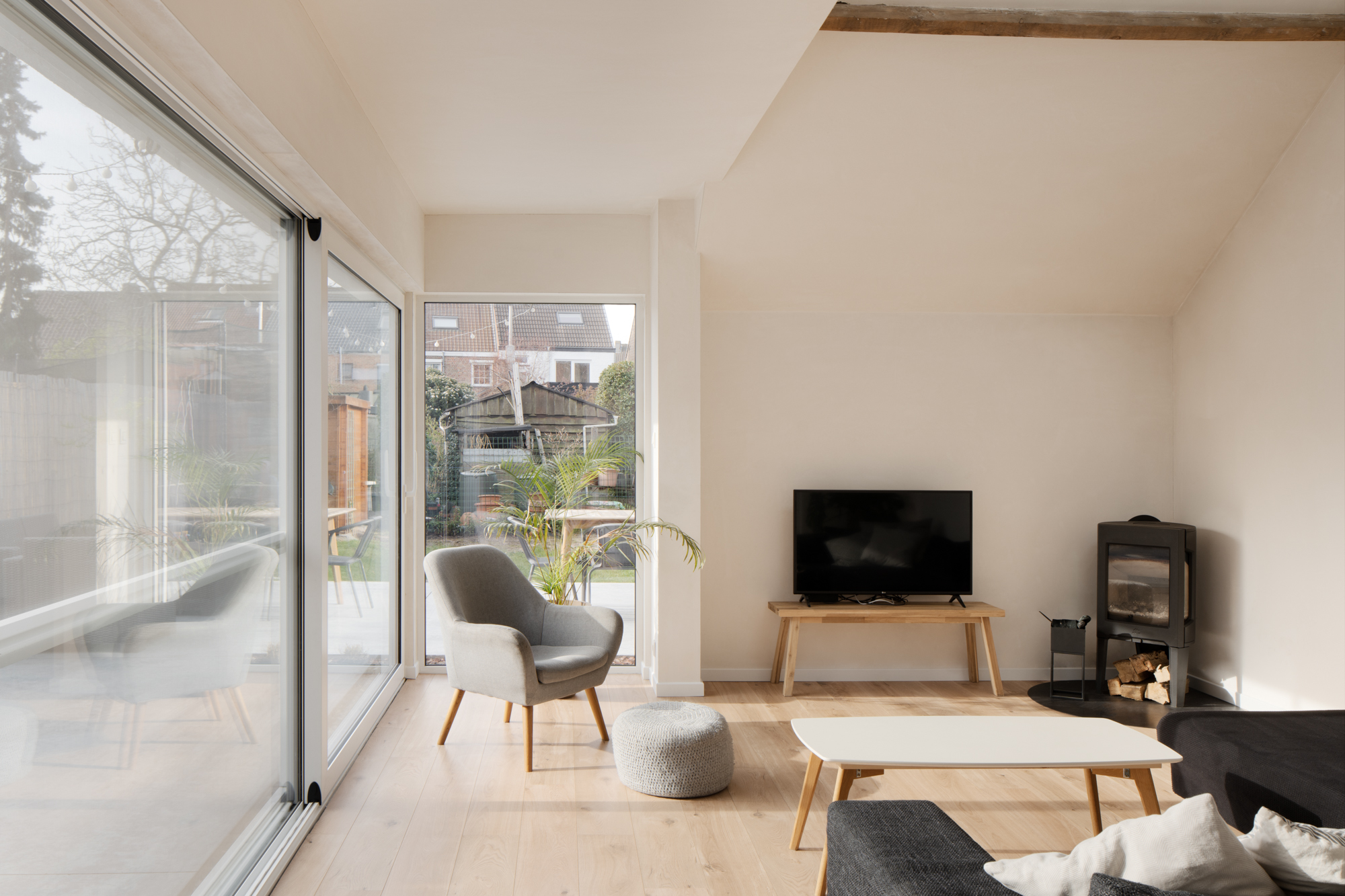 Lichte leefruimte in een gerenoveerde woning in gesloten bebouwing, met een groot vast ALU Visoglide Monorail-raam in mat verkeerswit en een moderne zithoek.