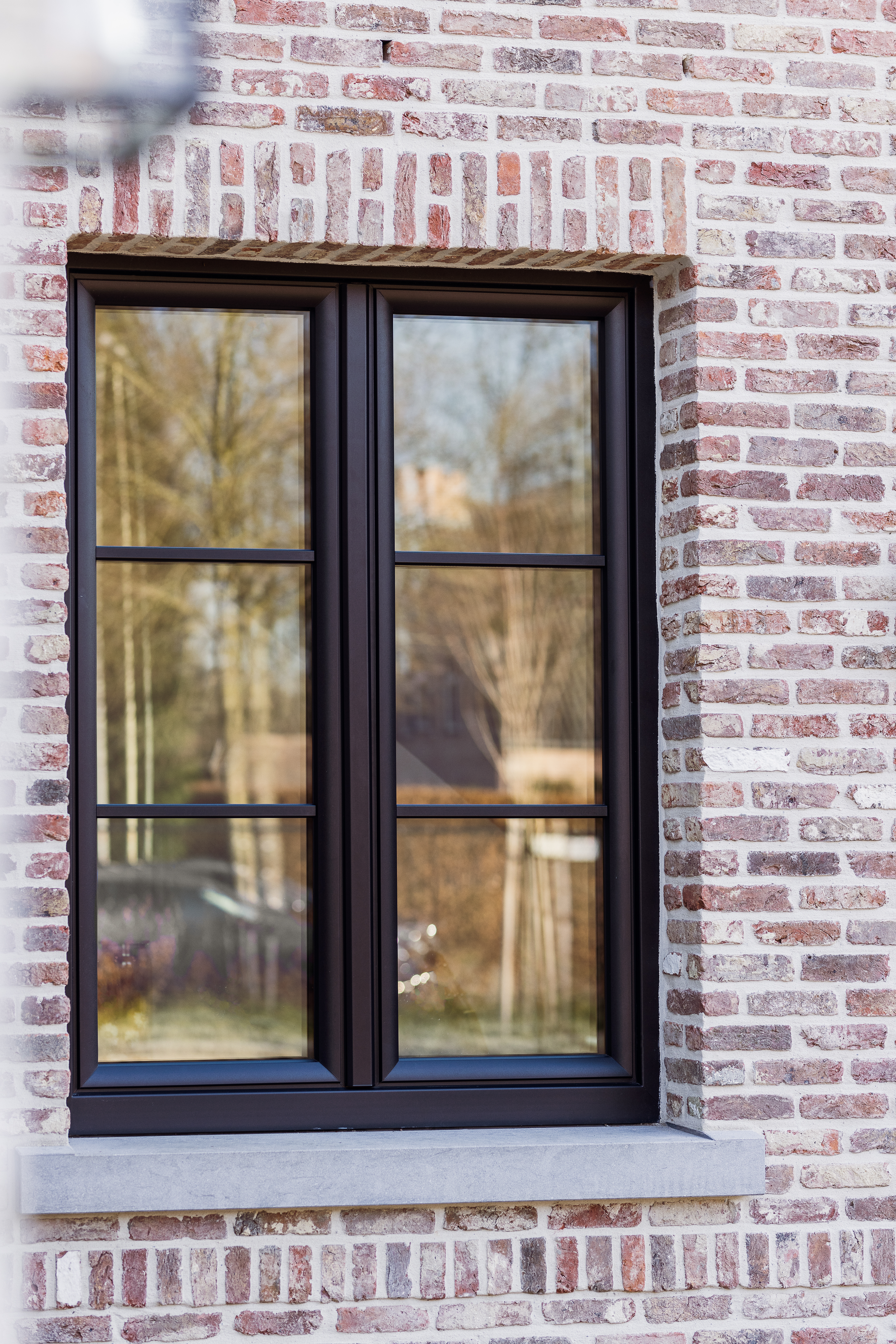 Mat zwart Impakt PLUS-raam met twee verticale delen en meerdere ruiten, geplaatst in een gevel met lichte bakstenen.