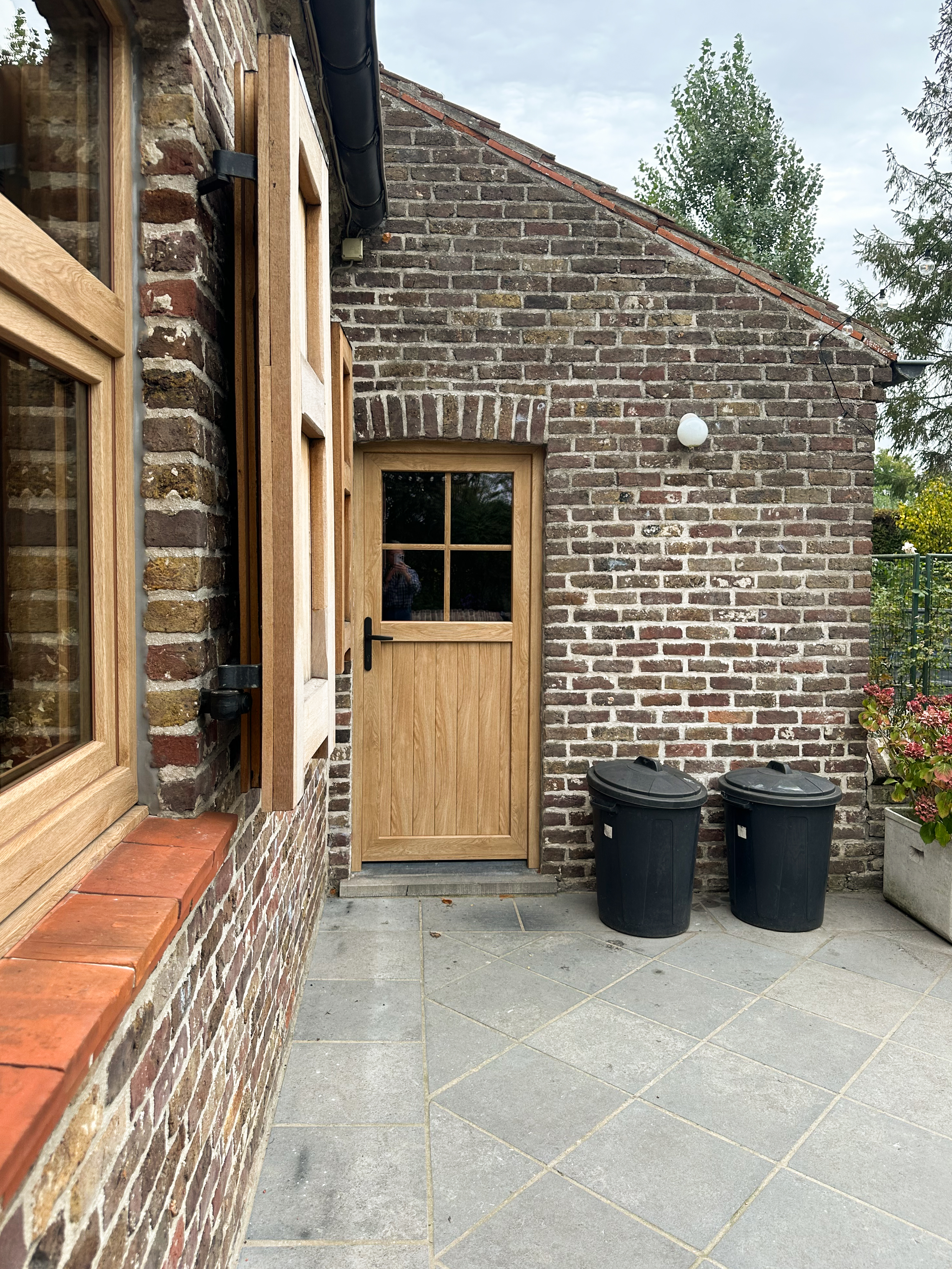 Halfbeglaasde pvc-deur in Woodec Eik Natuur NERF met glasverdeling, geplaatst in een bakstenen gevel naast een betegeld terras.