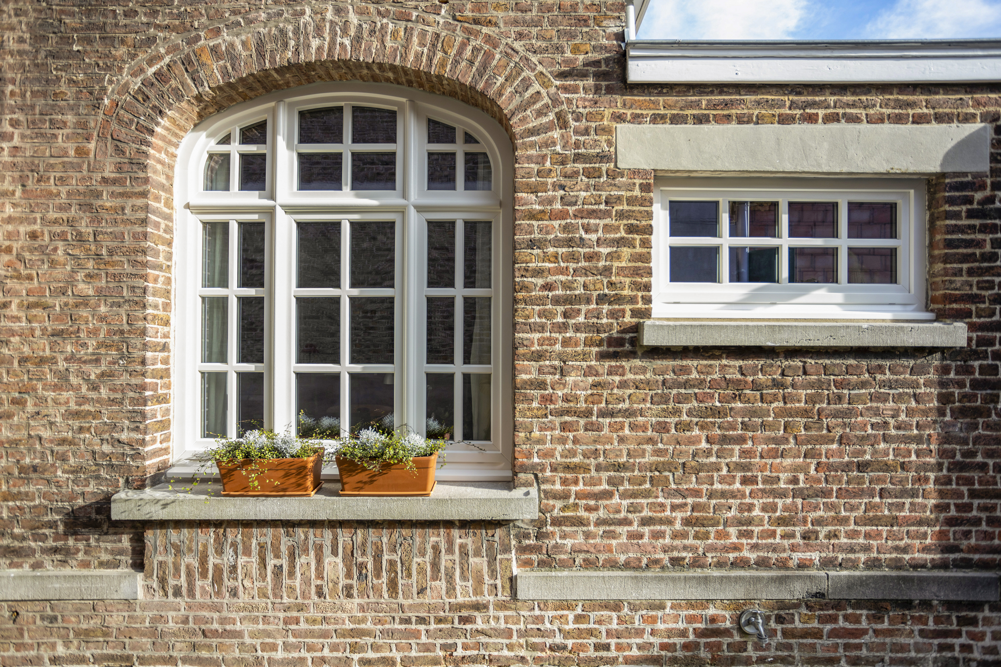 Bakstenen gevel met een gebogen draai-kipraam met bovenlicht en drie verticale delen, naast een kleiner raam.
