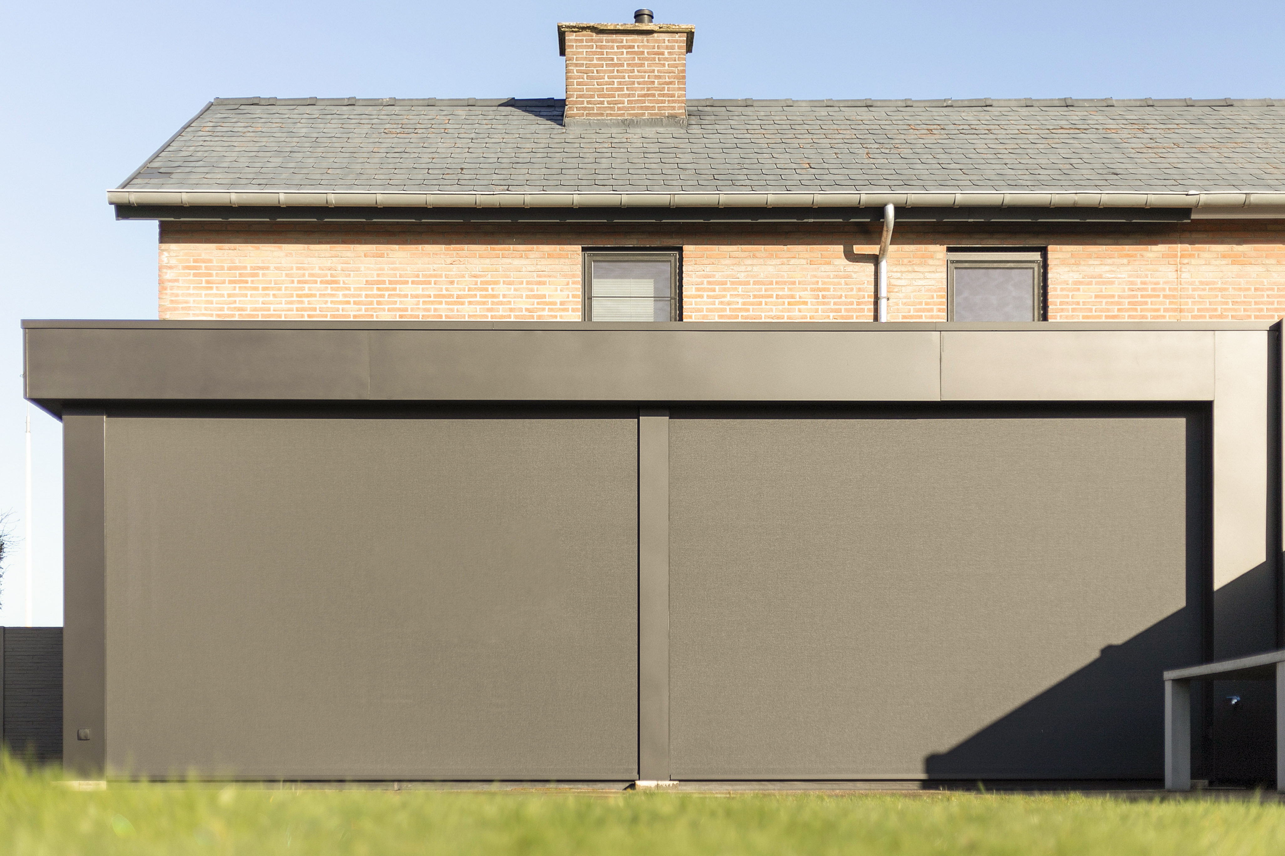 Donkergrijs vast raam met ingebouwde screen aan een gerenoveerde bakstenen woning in halfopen bebouwing, uitgevoerd in aluminium met een ALU Visoglide Duorail-profiel.