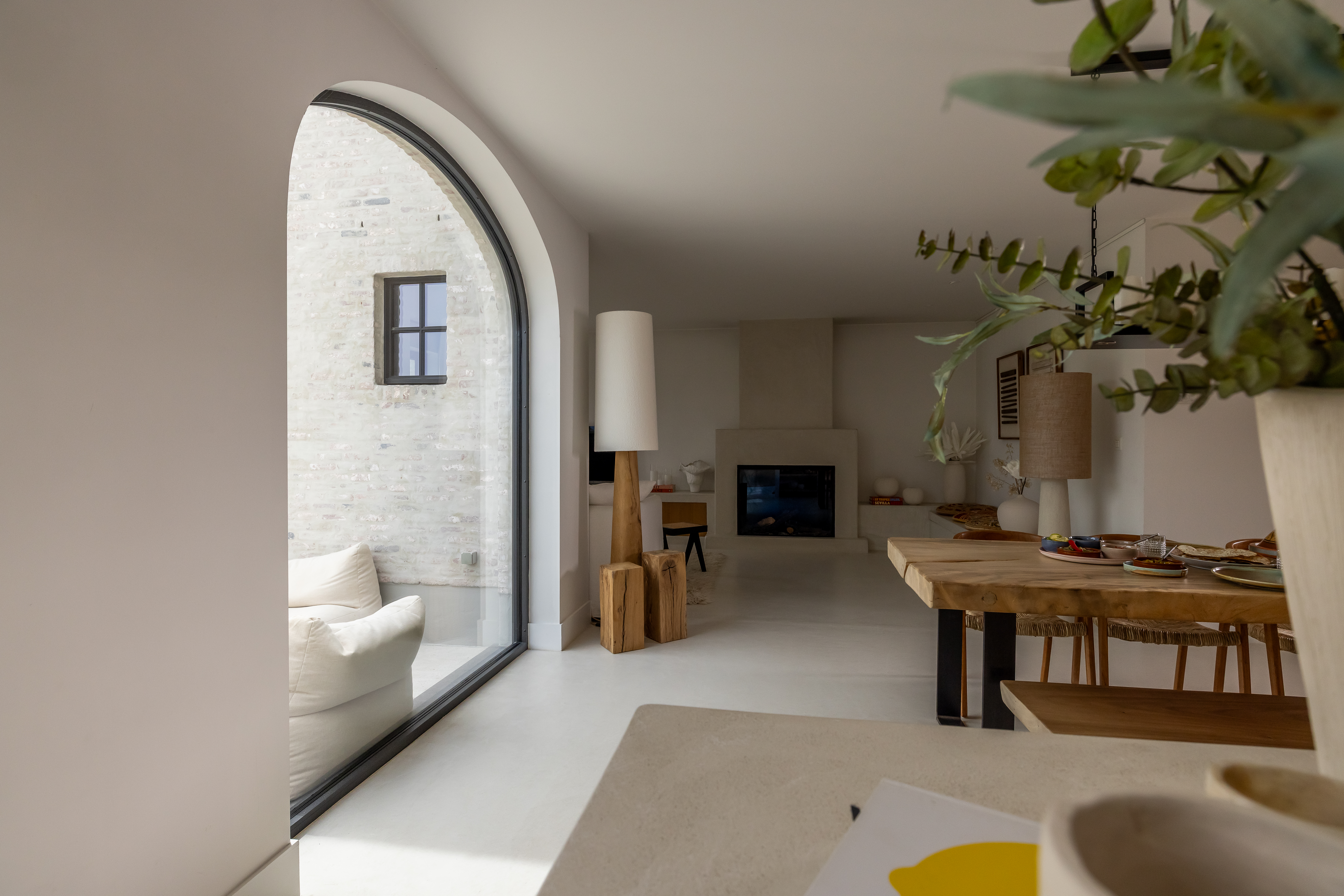 Groot vast raam in Steellook met slanke zwarte profielen en een afgeronde boog, in een warm landelijk ingericht leefgedeelte van een nieuwbouwwoning.