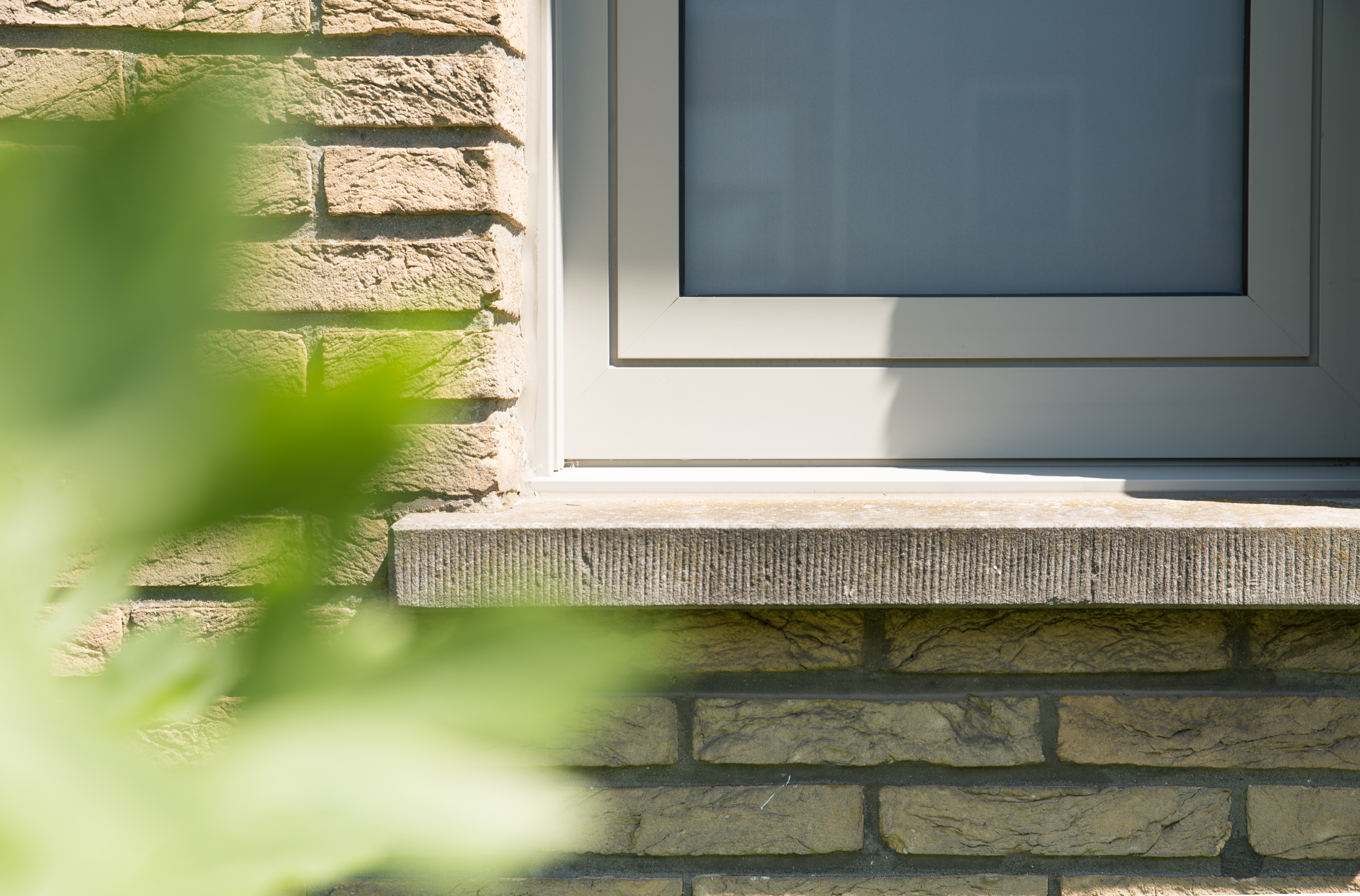 Close-up van een licht raam met brede vensterbank in de natuurstenen gevel van een gerenoveerde driegevelwoning.