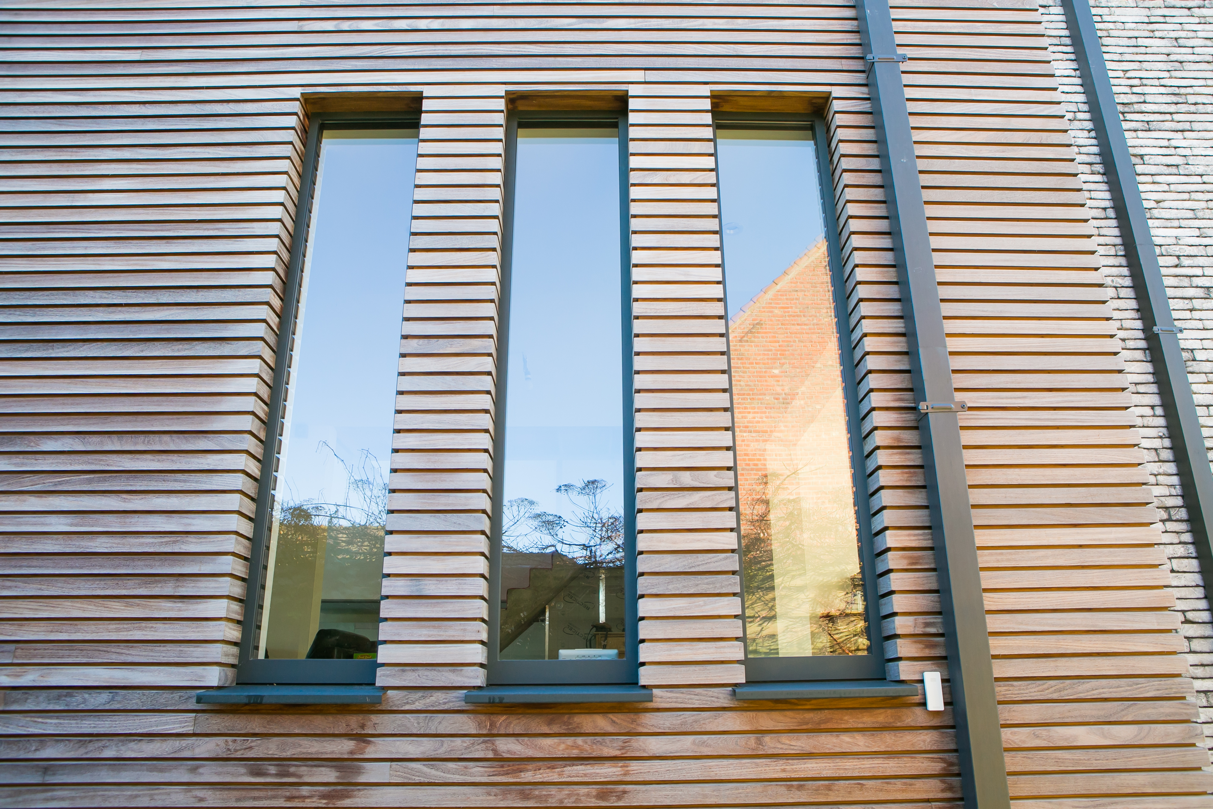 Modern vast raam in zwartgrijze uitvoering met drie hoge glasvlakken, geïntegreerd in een horizontaal beklede gevel van een nieuwbouwwoning.