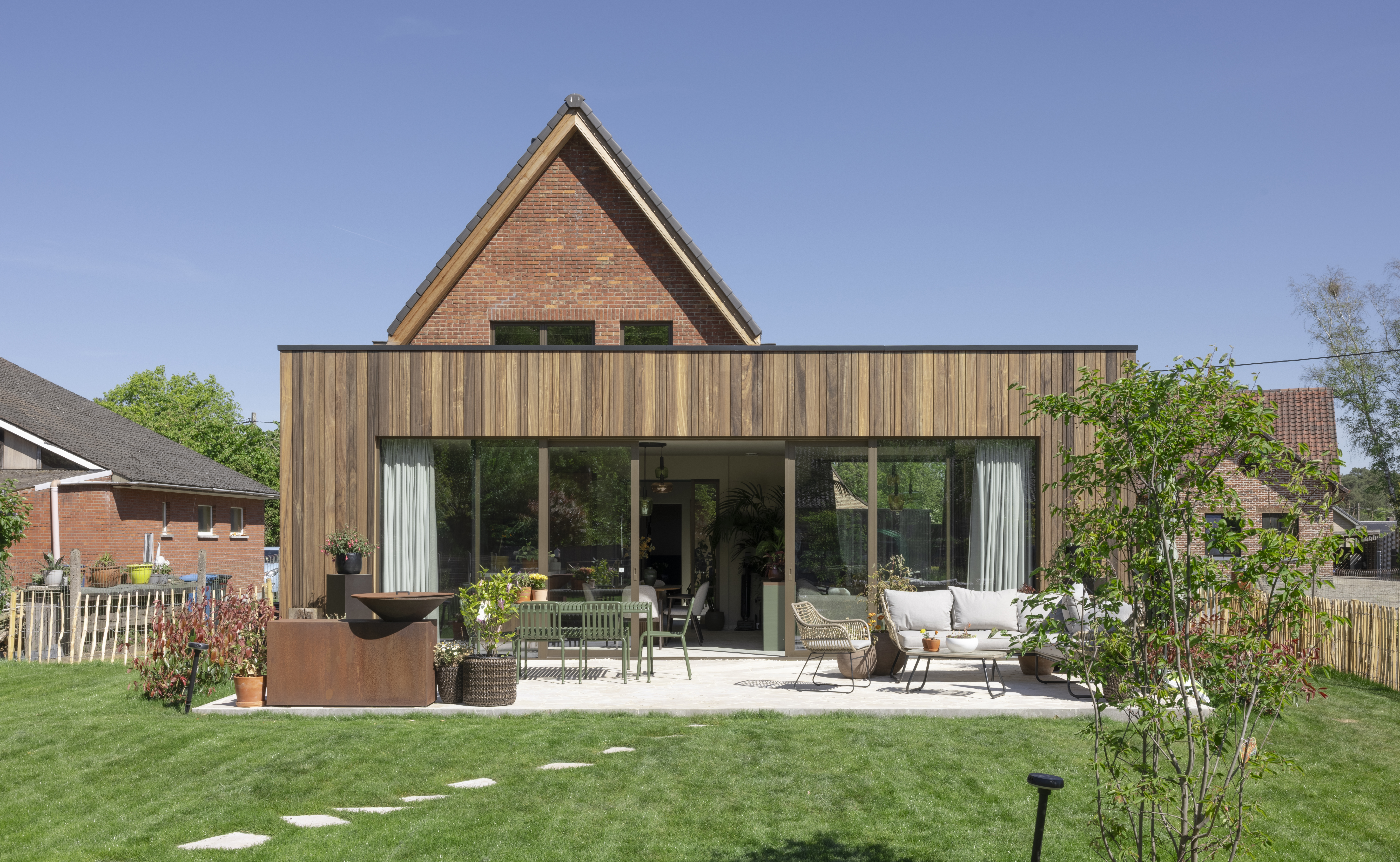 Hedendaagse aanbouw met groot aluminium schuifraam in C33-bronsanodisatie, uitgevoerd als ALU Visoglide Monorail, aan een woning met houten gevelbekleding en terras.