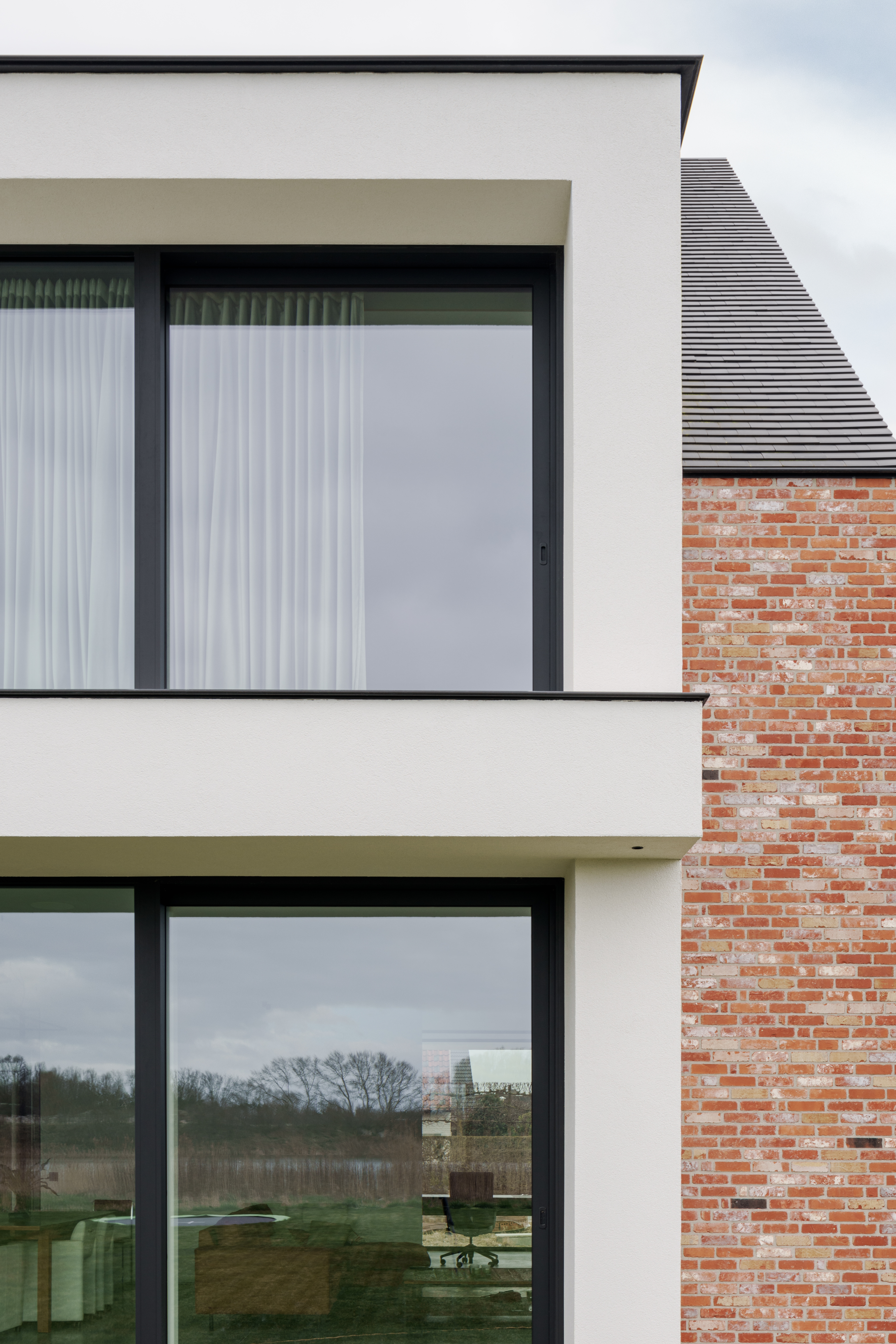 Moderne nieuwbouwwoning met grote zwarte aluminium schuiframen in een witte gevel, naast een rode bakstenen zijgevel.