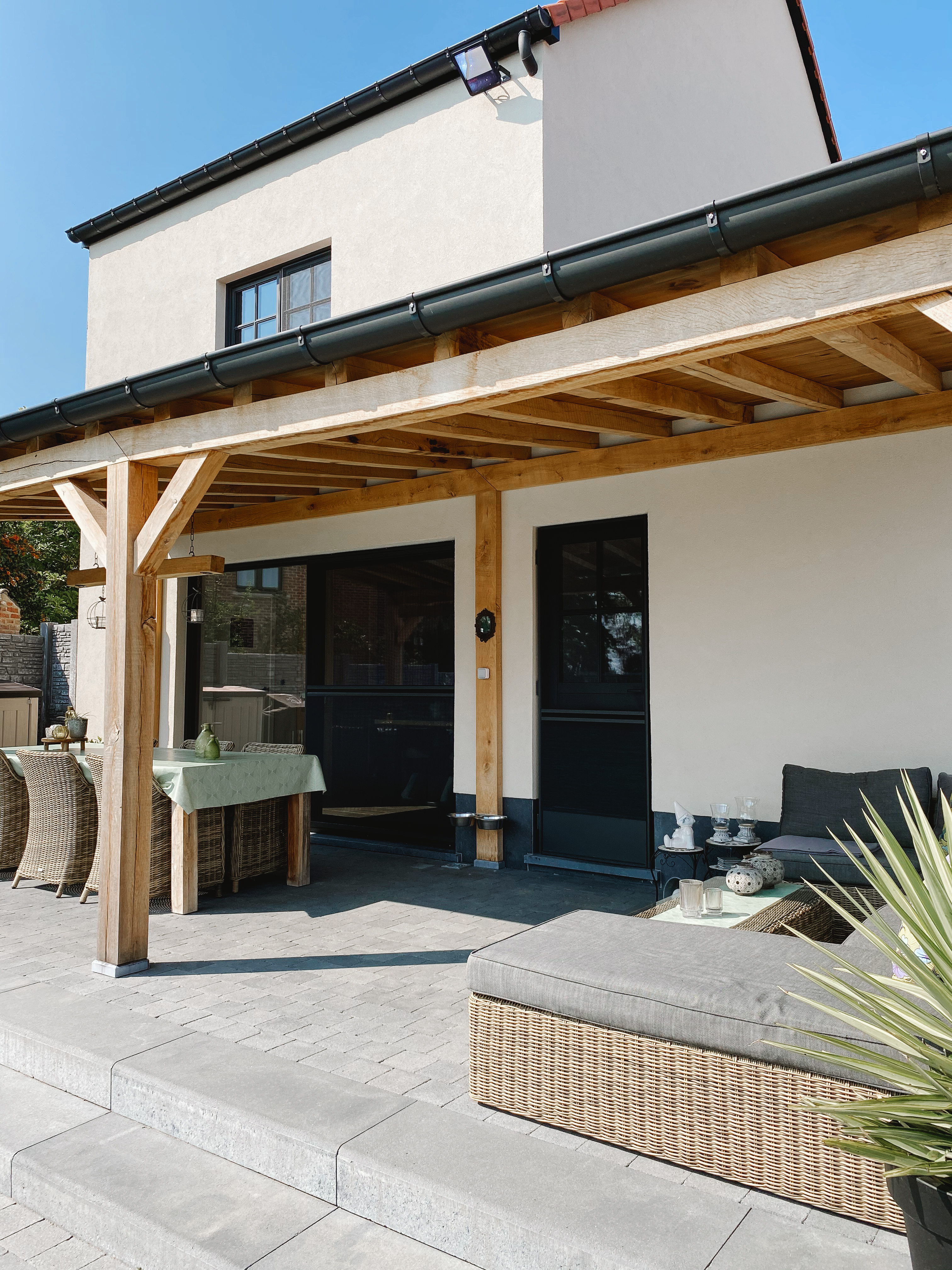 Zwarte Steellook PLUS small-raamprofielen en deuren aan een gerenoveerde vrijstaande woning met landelijke uitstraling, onder een houten overkapping met terras en tuinmeubilair.