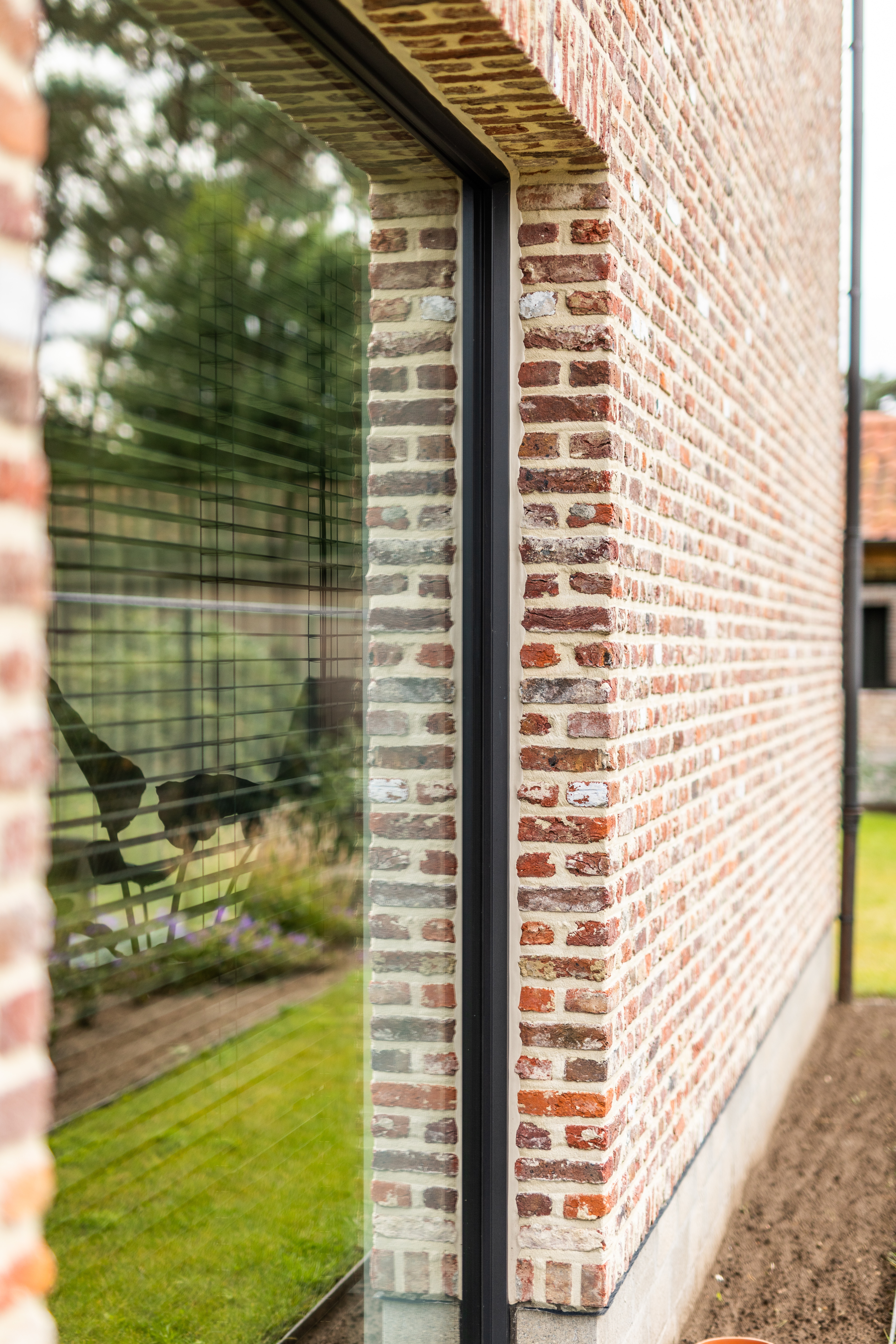 Vast, bijna kamerhoog raam met slank Steellook-profiel in de warme, landelijke bakstenen gevel van een nieuwbouwwoning in open bebouwing.