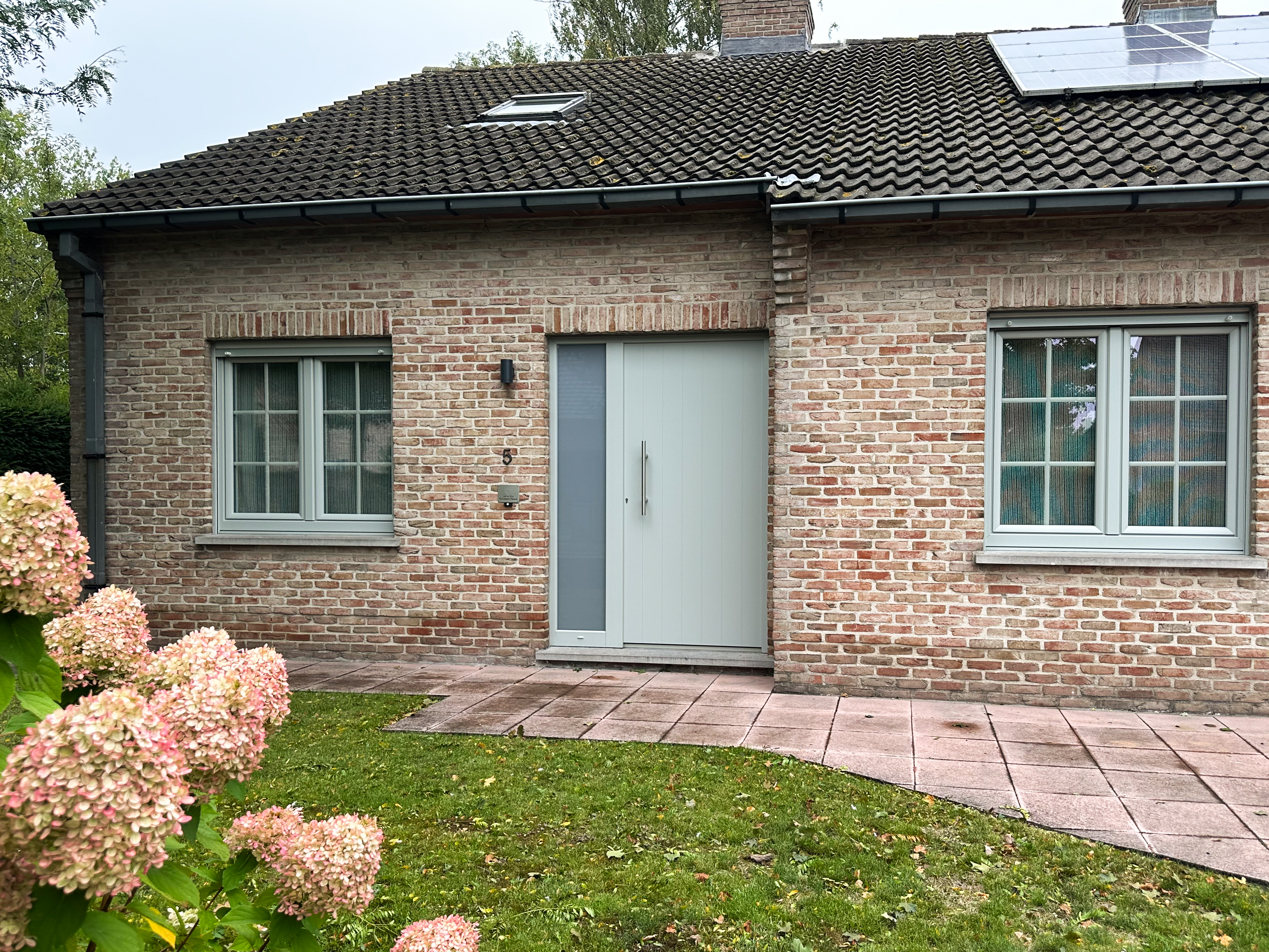 Agaatgrijze PVC-ramen met draai-kipfunctie en een grijze deur met zijlicht en paneel in de bakstenen gevel van een woning.