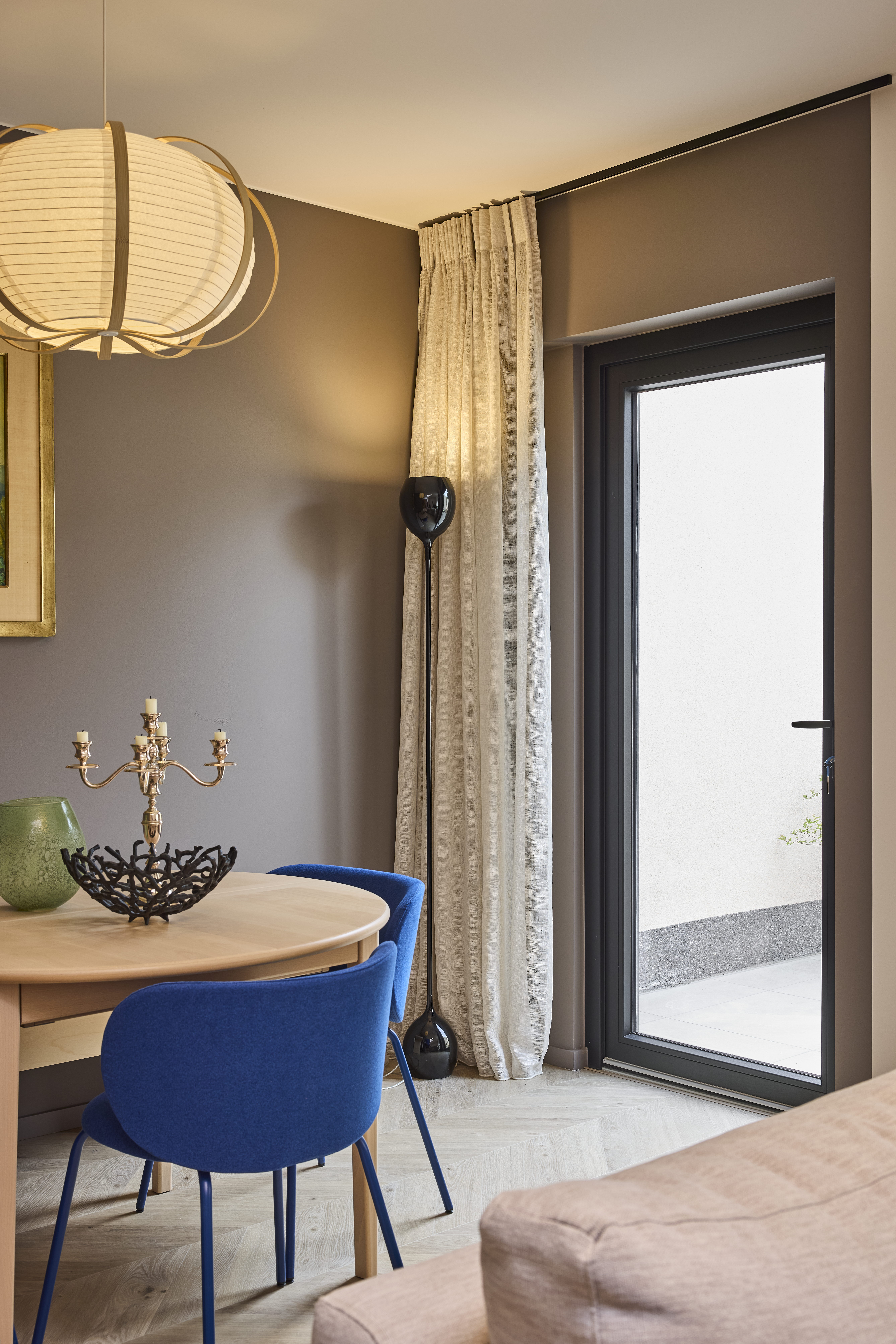 Interieur met een matzwarte beglaasde PVC Komfort PLUS-deur, lange gordijnen, een eettafel en blauwe stoelen.