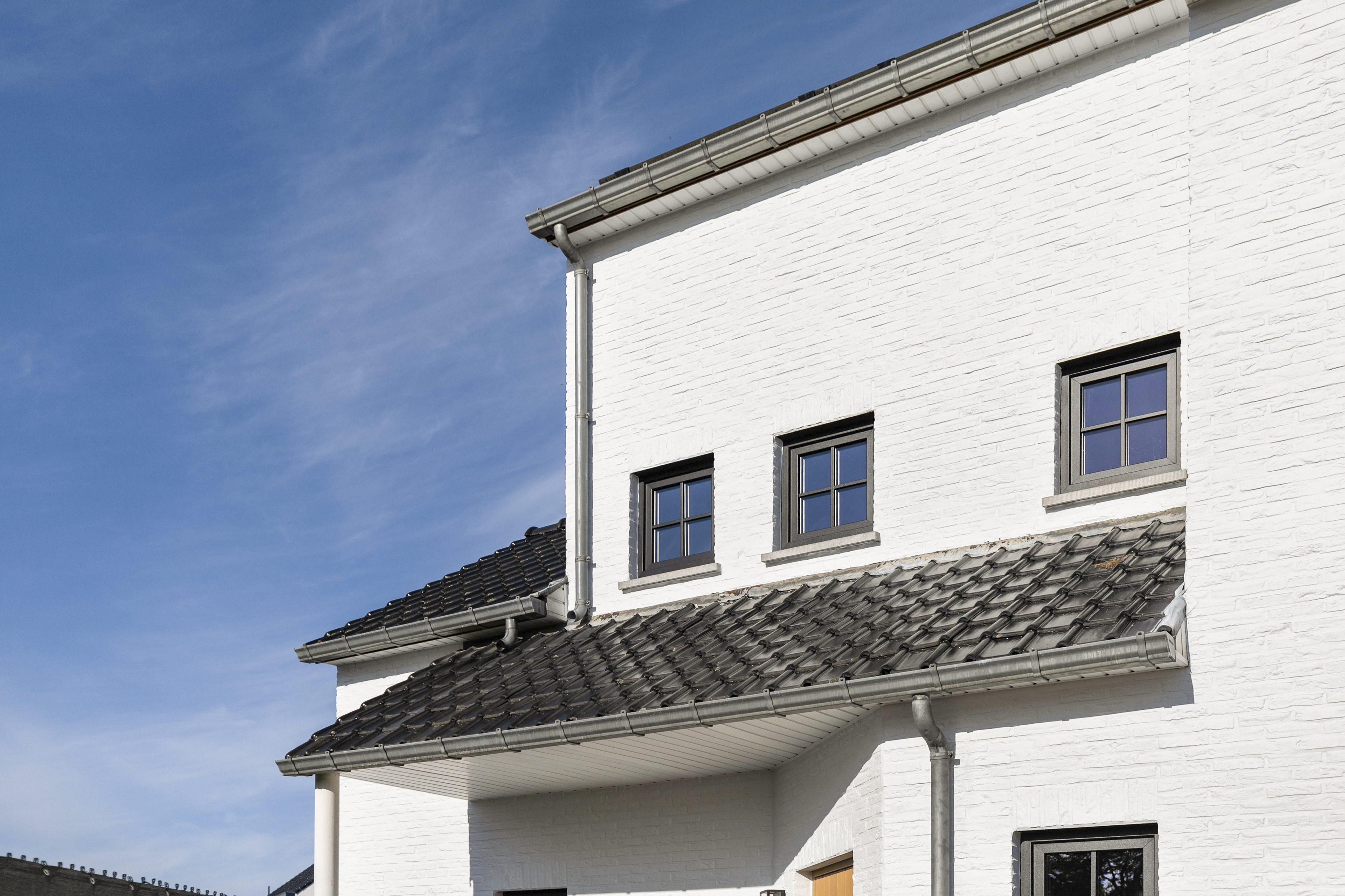 Witte voorgevel van een halfopen woning met matzwarte draai-kipramen, een hellend pannendak en een uitstekende dakrand.