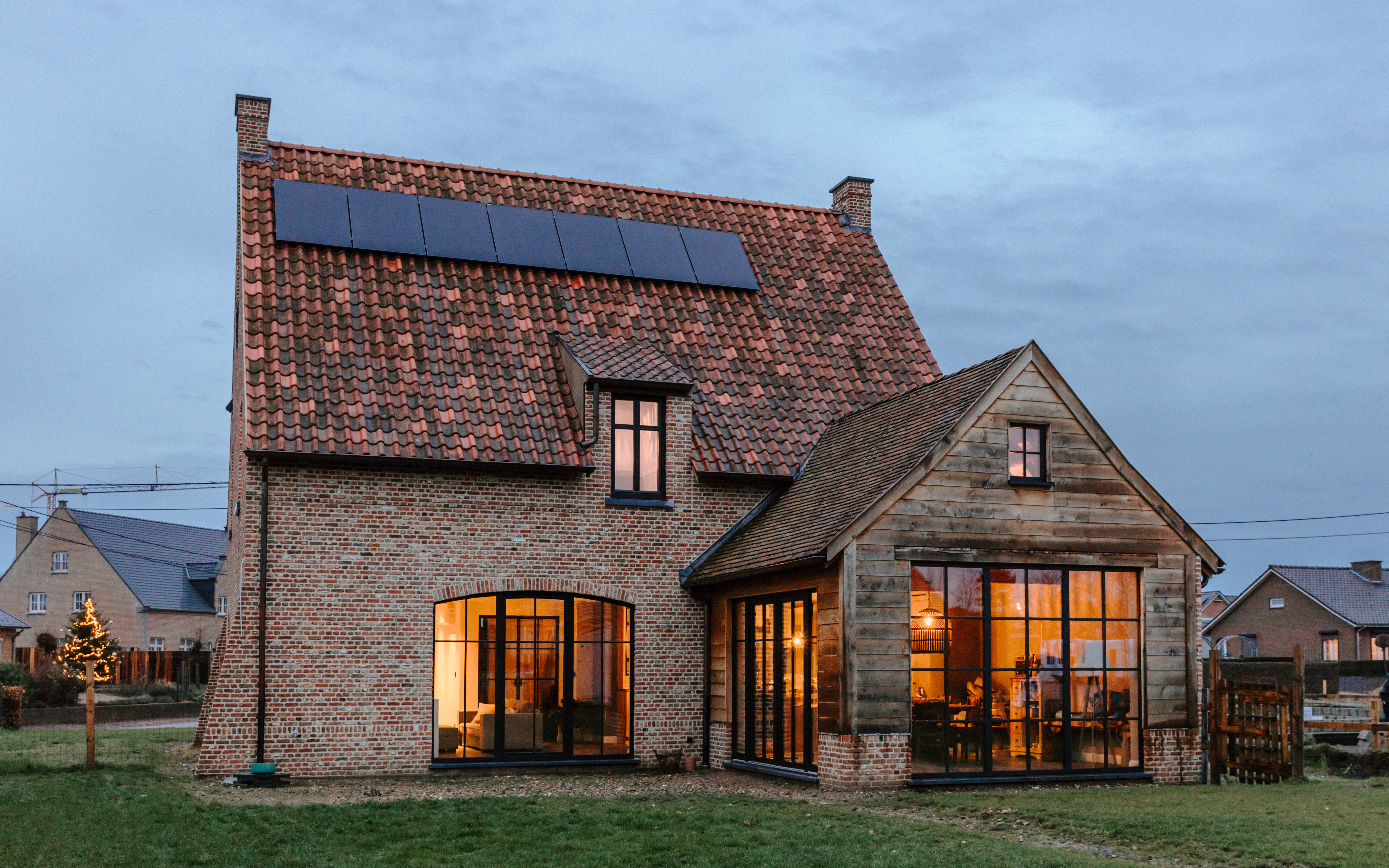 Landelijke vrijstaande woning met matzwarte Impakt PLUS rond- en Koncept-ramen, waaronder vaste en draai-kipramen, warm verlicht bij valavond.