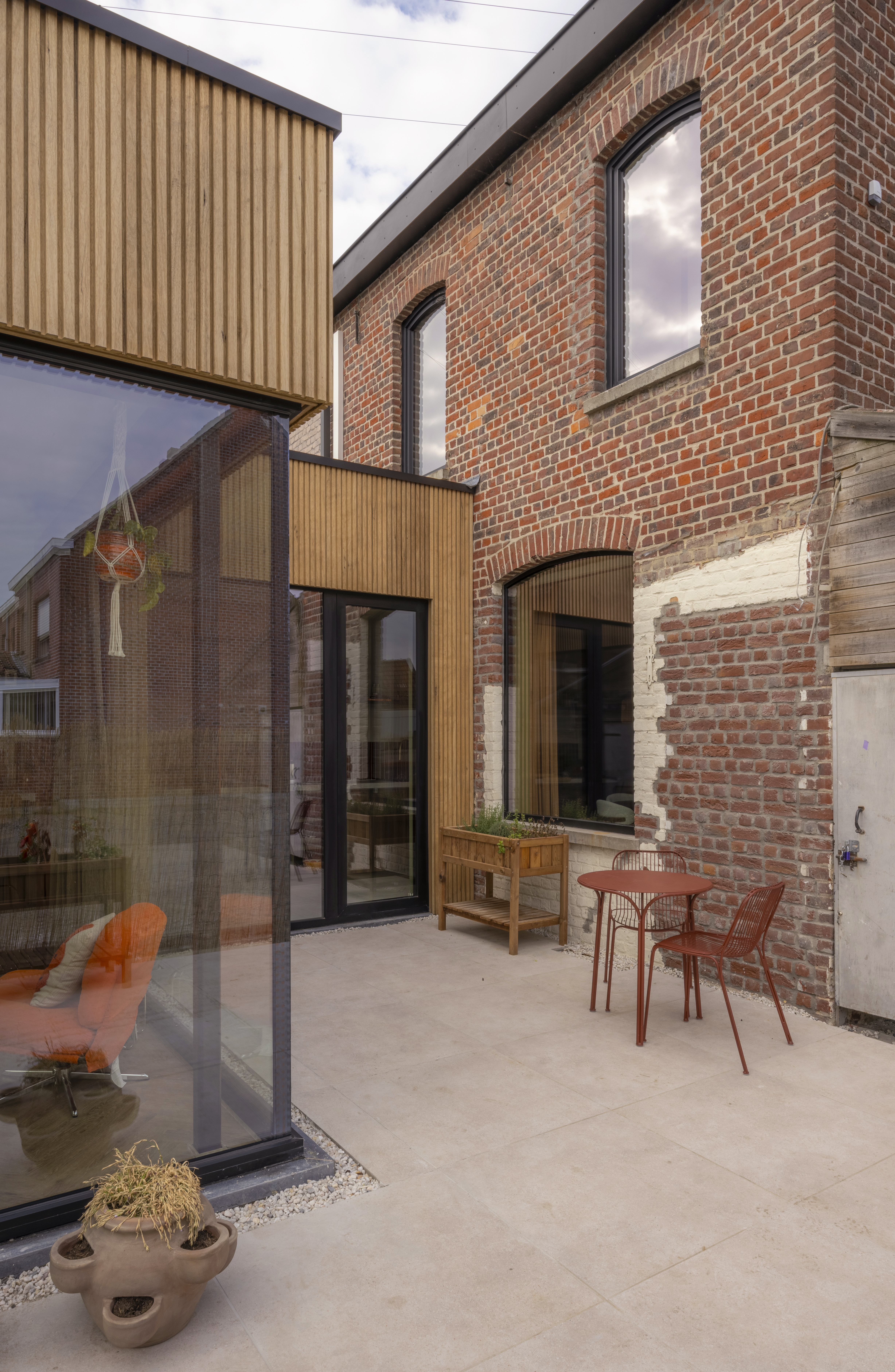 Binnenkoer van een bakstenen gebouw met grote glaspartijen en diepzwarte raamprofielen uit de Komfort-reeks, met een vast raam en een draai-kipraam.