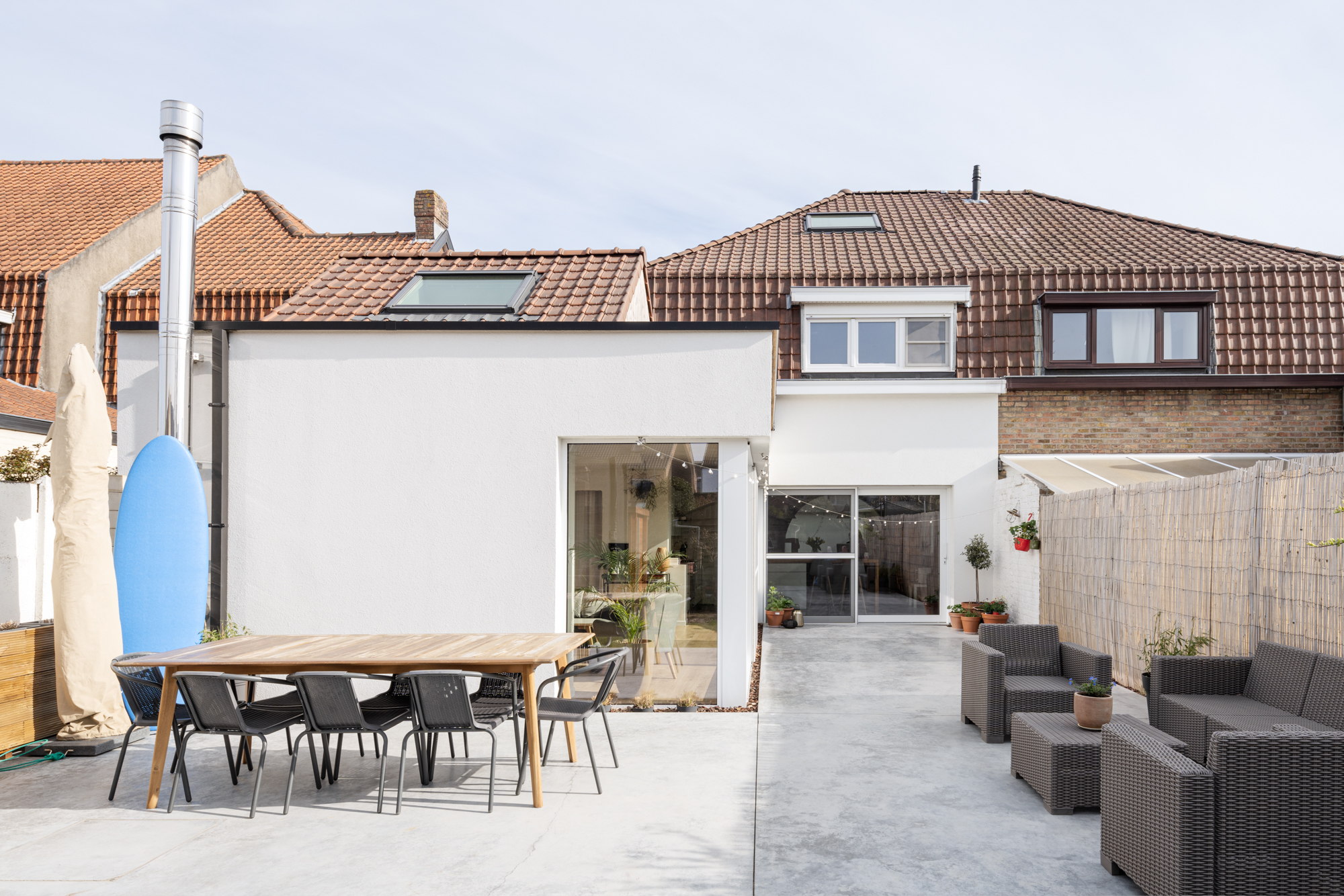 Gerenoveerde gesloten bebouwing met een vast raam in verkeerswit, een lichte gevel en een ruim terras met eettafel en tuinmeubilair.