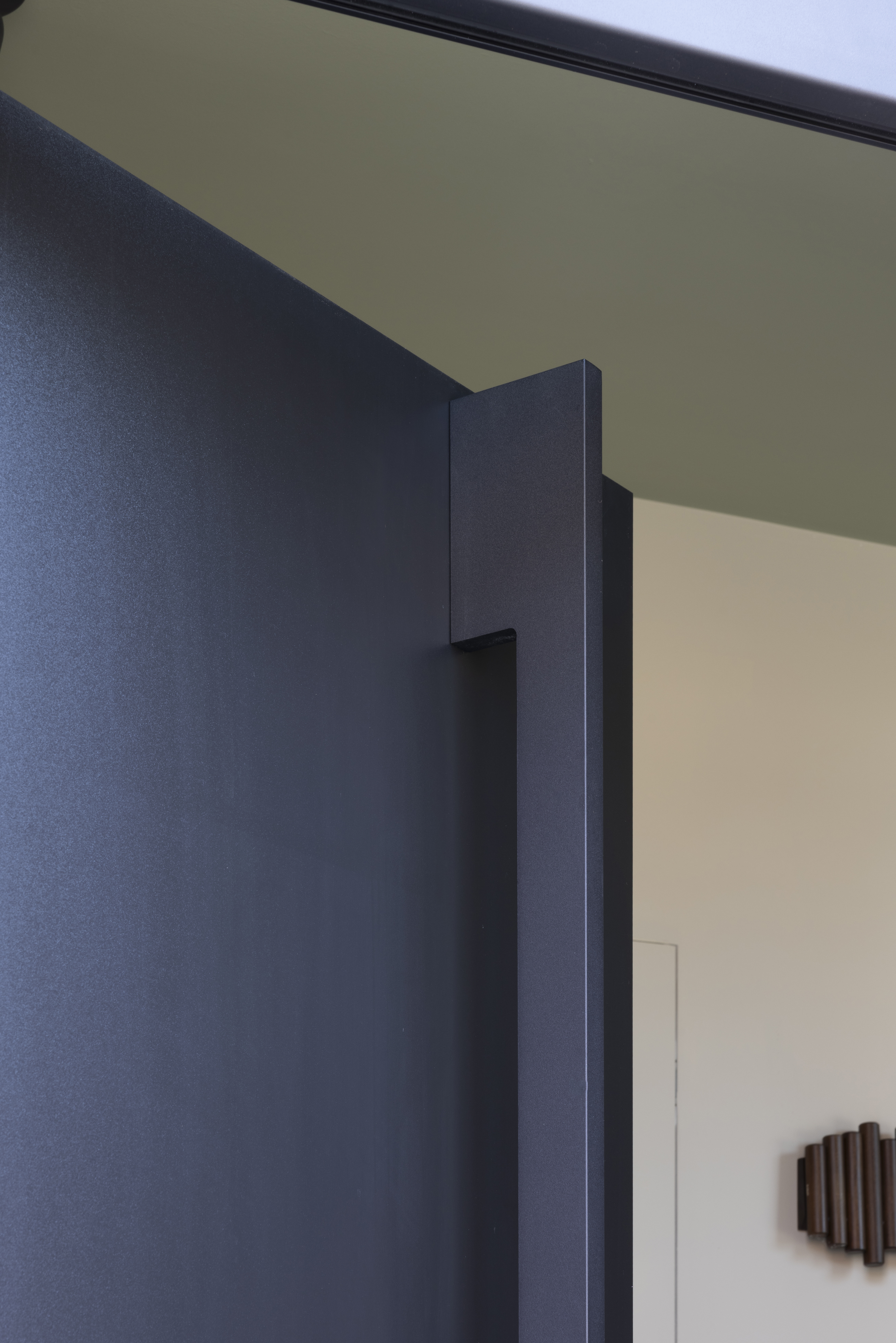 Matte zwarte PVC-deur met bovenlicht en paneel, openstaand in een modern interieur met donkere wand en lichte plafondafwerking.