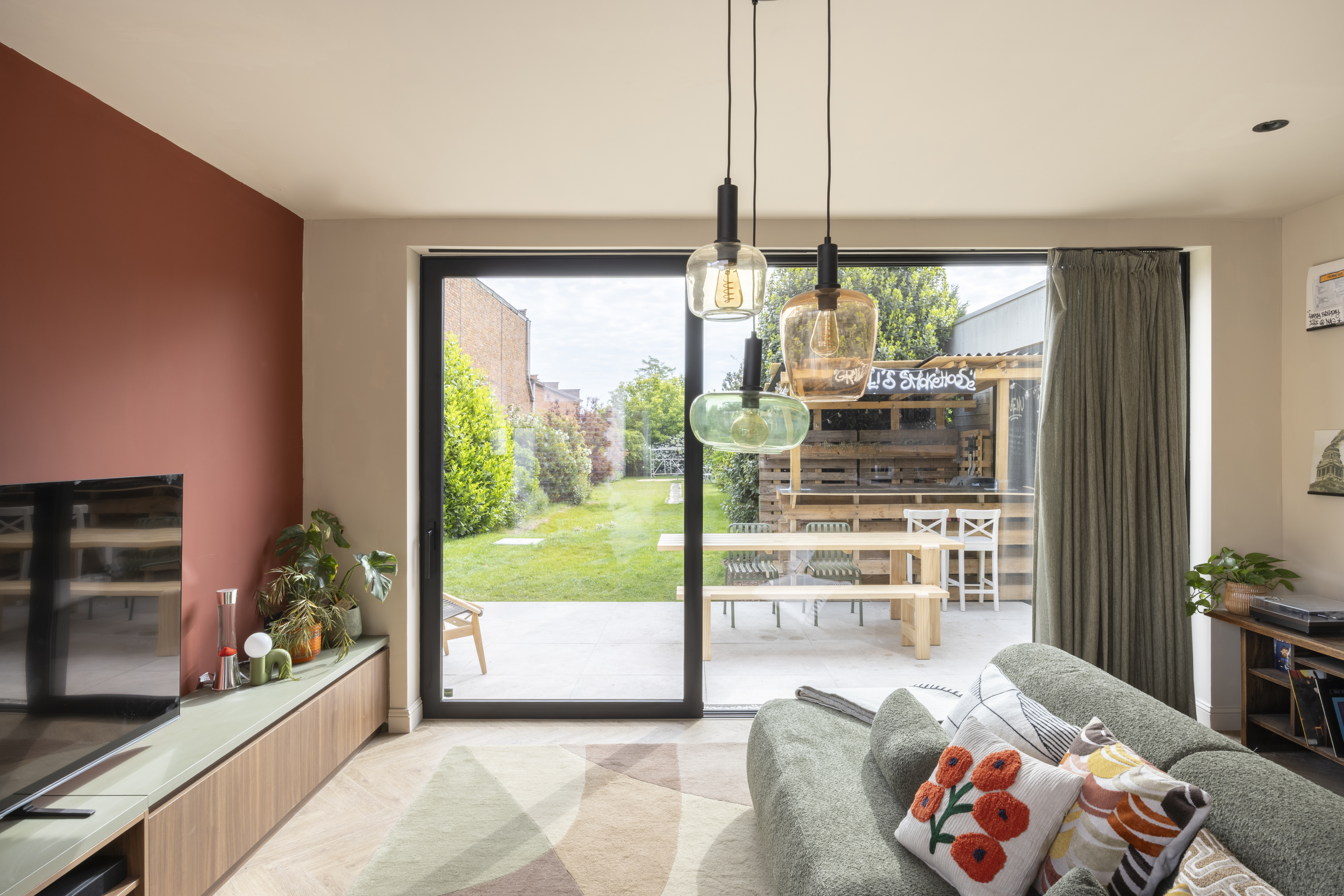 Zwart aluminium schuifraam ALU Visoglide Monorail in een lichtrijke leefruimte, met zicht op het groene terras en de tuin.