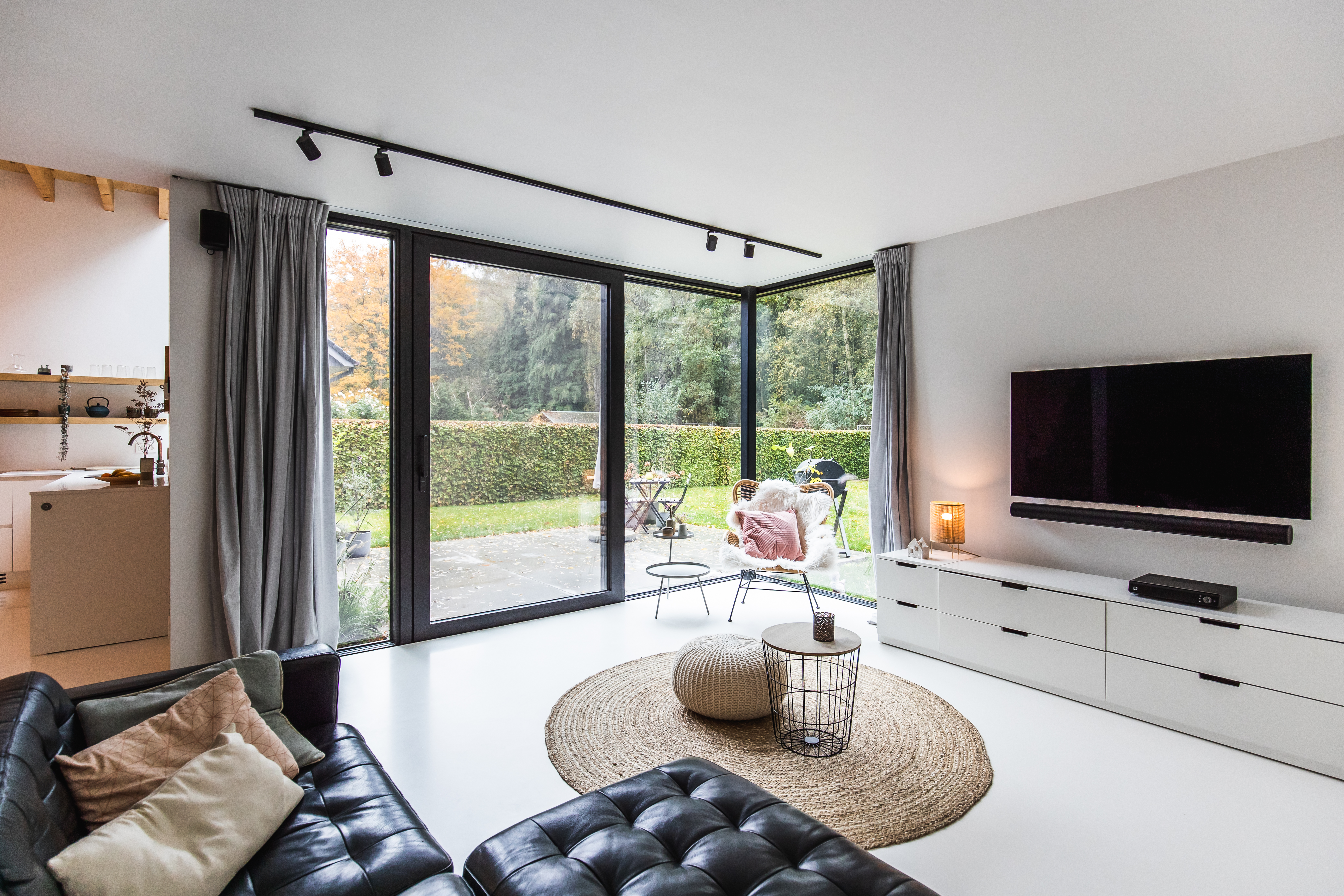 Modern interieur van een vrijstaande nieuwbouwwoning met een zwart ALU Visoglide Monorail-schuifraam naar de tuin, naast een zithoek en keuken.