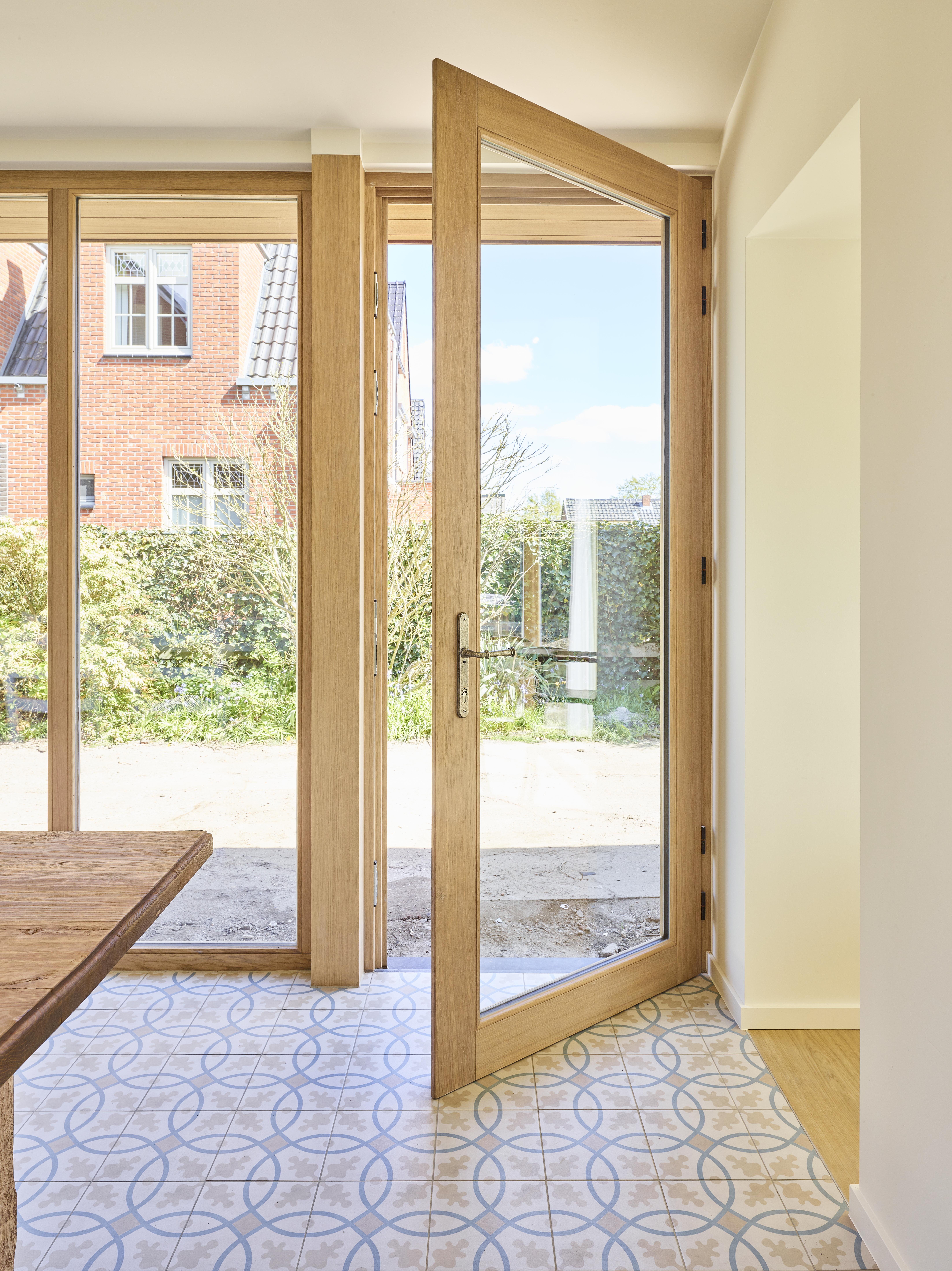 Open beglaasde deur in afgelakte lichte eik, met een warme landelijke uitstraling, die uitkijkt op de tuin en een vloer met patroon binnen.