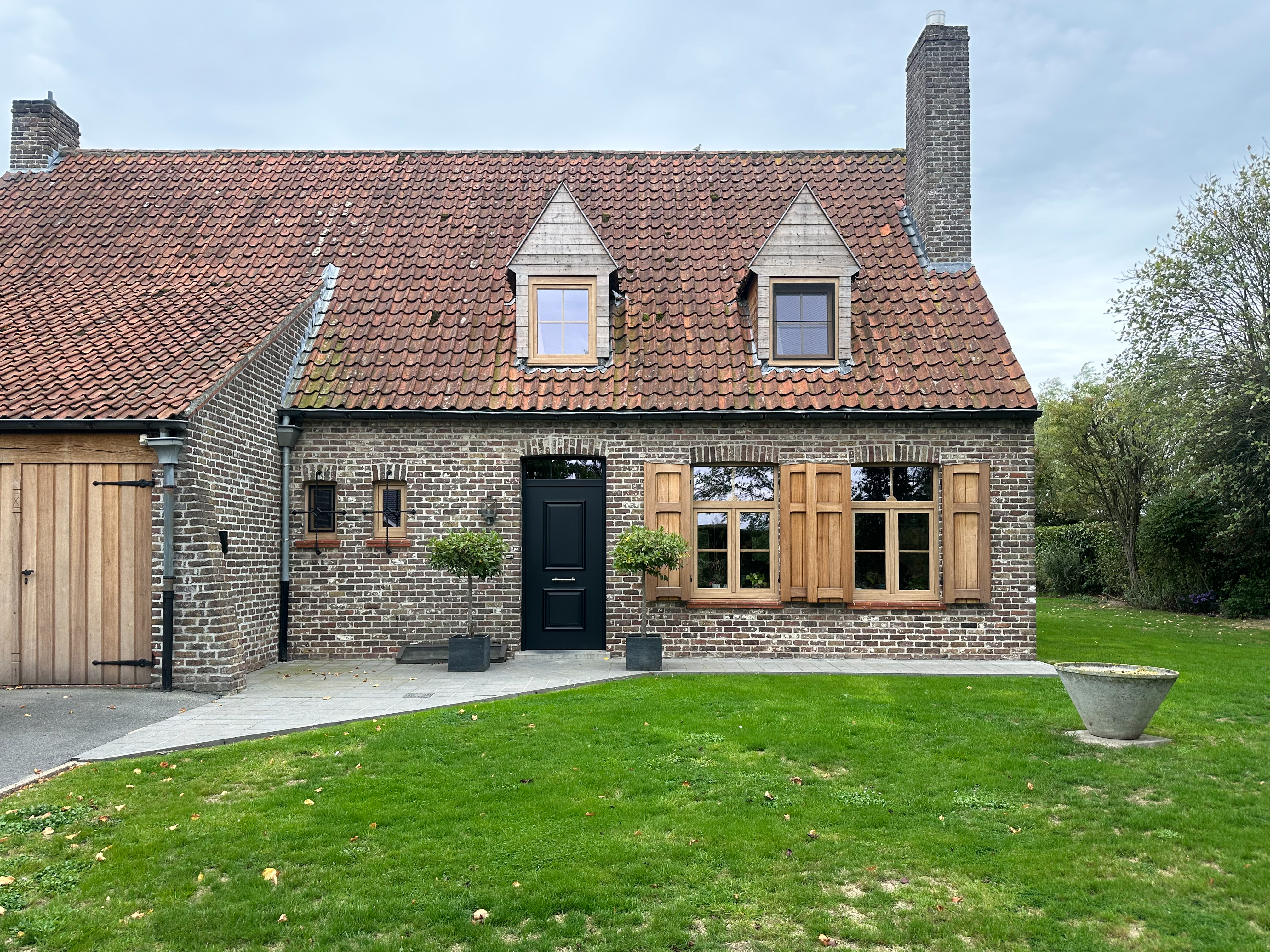 Traditionele bakstenen woning met zwarte voordeur en pvc-ramen in natuurlijke eiklook, waaronder een dubbel raam met bovenlicht en draai-kipfunctie.