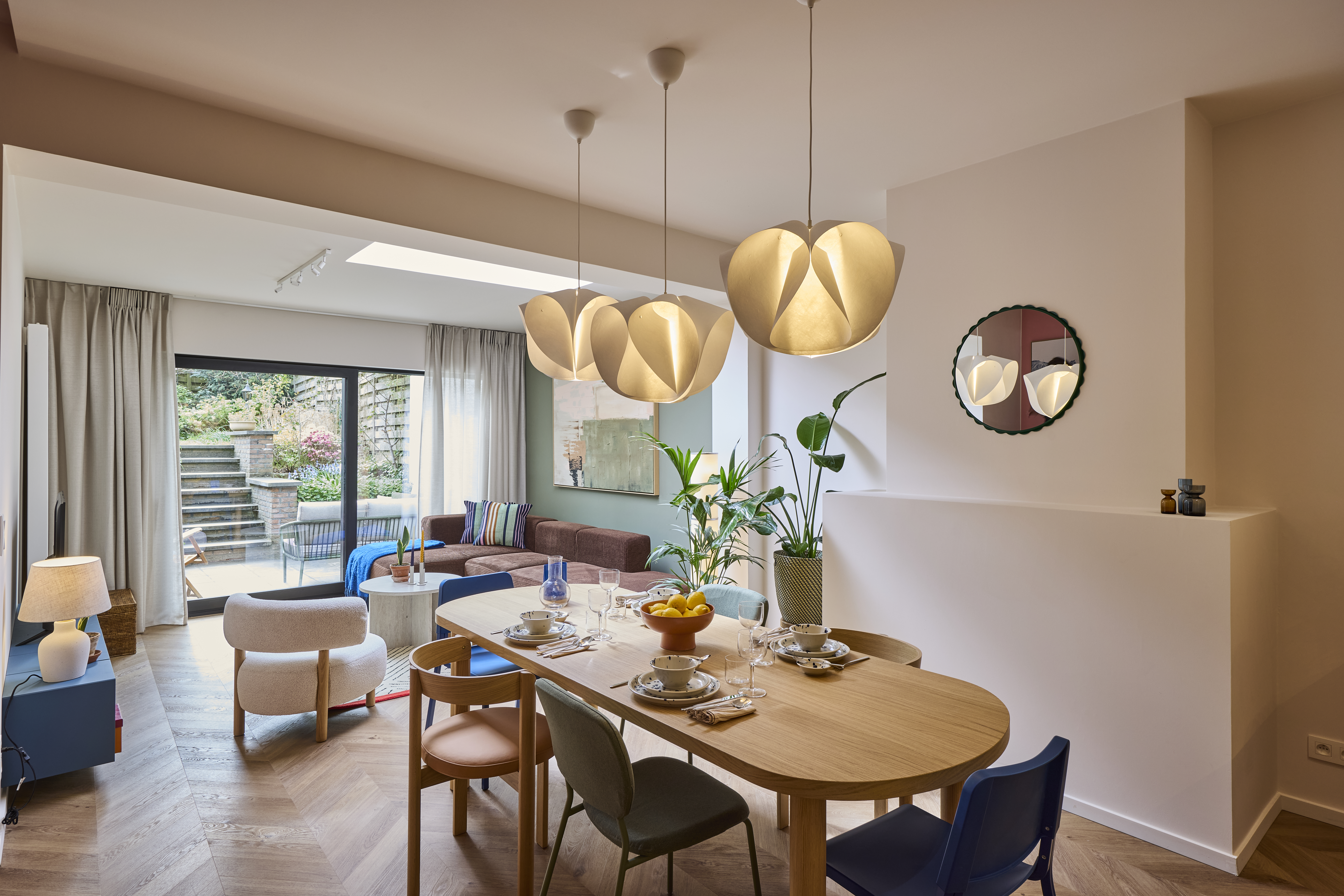 Lichte eetruimte met houten tafel, planten en een ALU Visoglide Monorail-schuifraam in signaalzwart naar een groene buitenruimte.